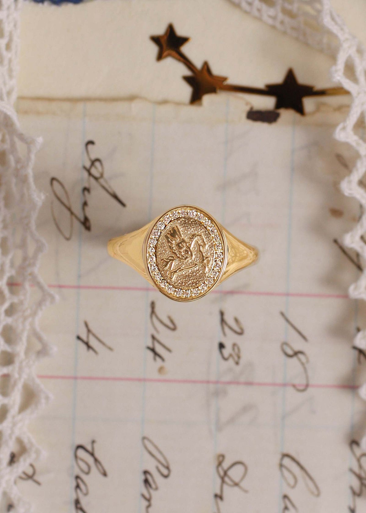 A Kinn 14k Gold Pegasus Dream Diamond Signet Ring sitting upright against a letter