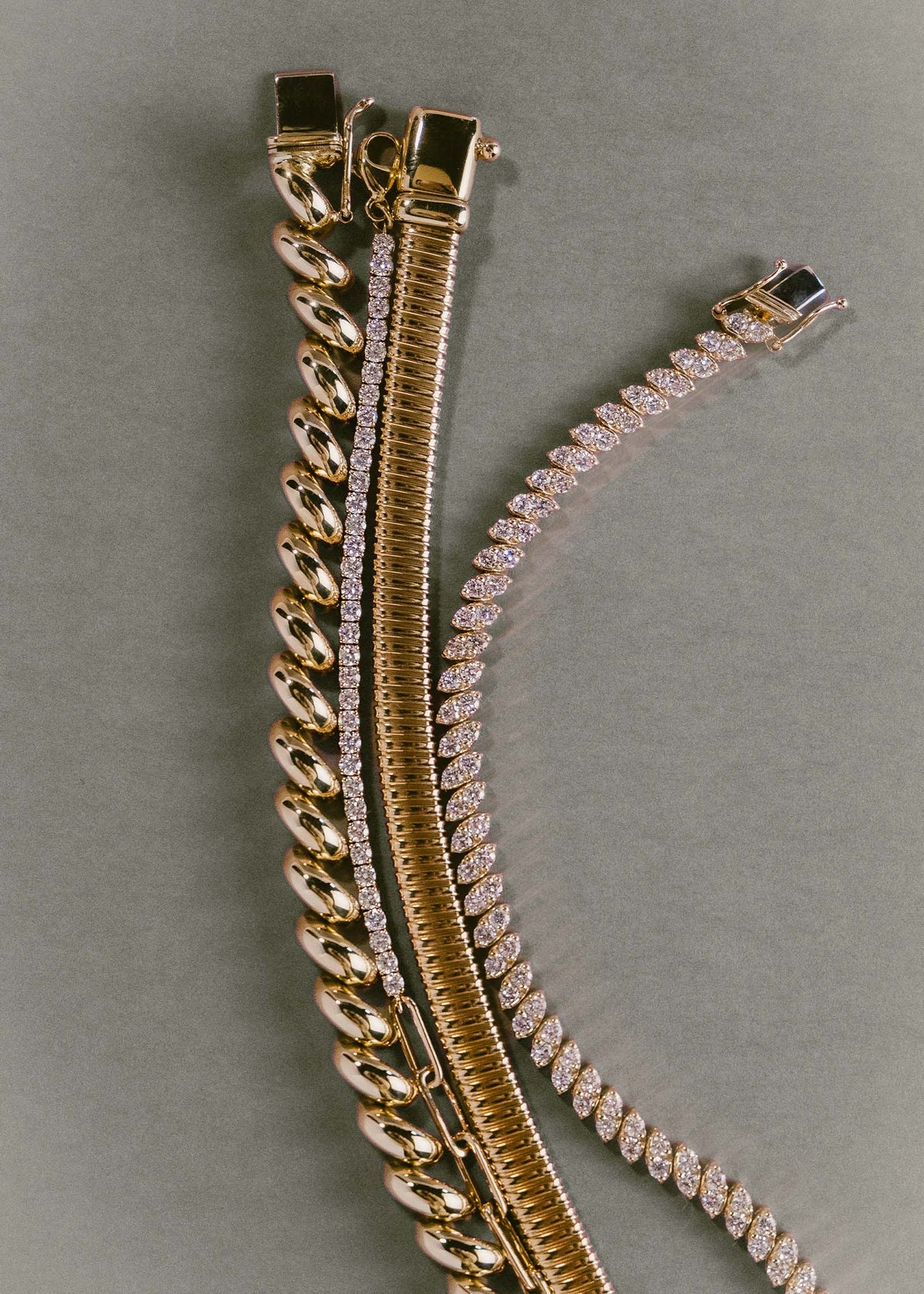 A Kinn Studio 14k Gold Hampshire House Bracelet with a Coco Round Tennis Link Bracelet Diamond, Celina Tubogas Bracelet, and a Sofia Diamond Marquise Bracelet laying together flat against a light blue background