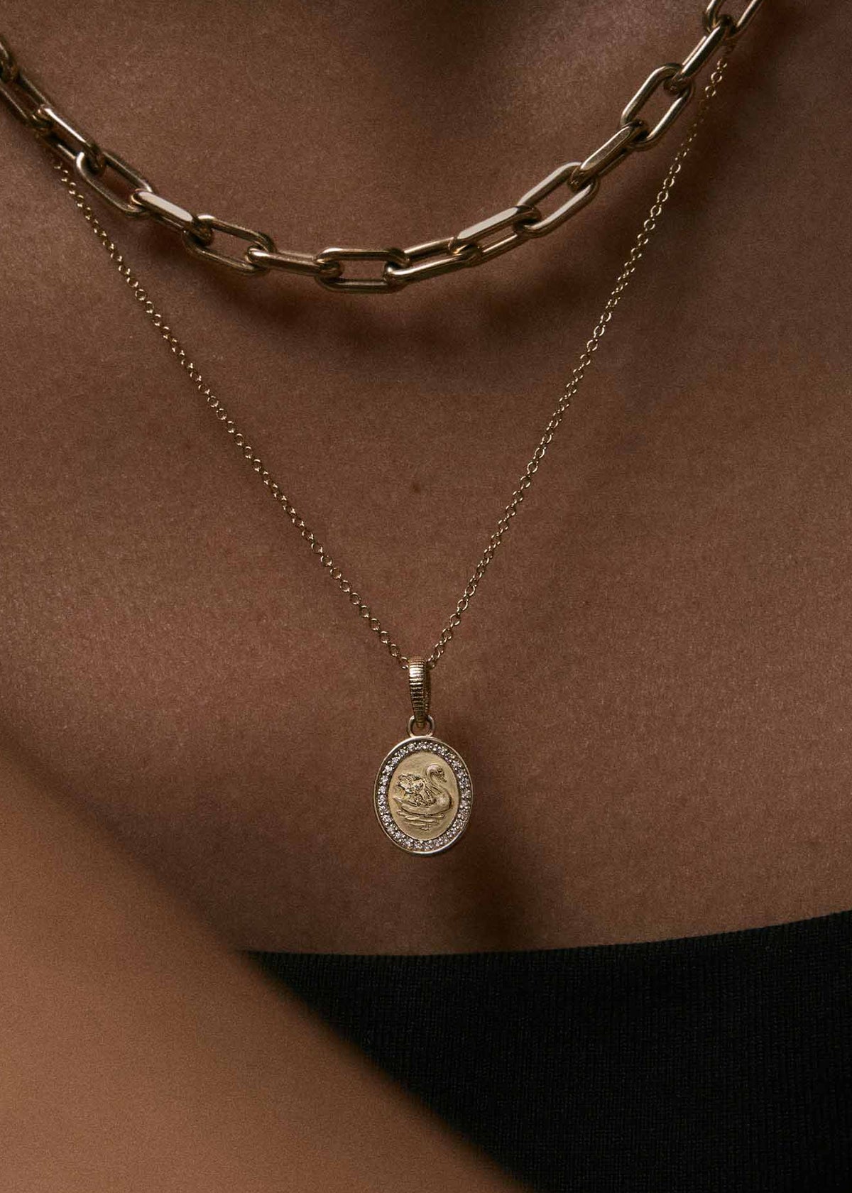 A close-up of a model wearing a Kinn 14k Gold Swan Dream Diamond Pendant on a Micro Rolo Chain Necklace layered with a Mia Link Chain Necklace