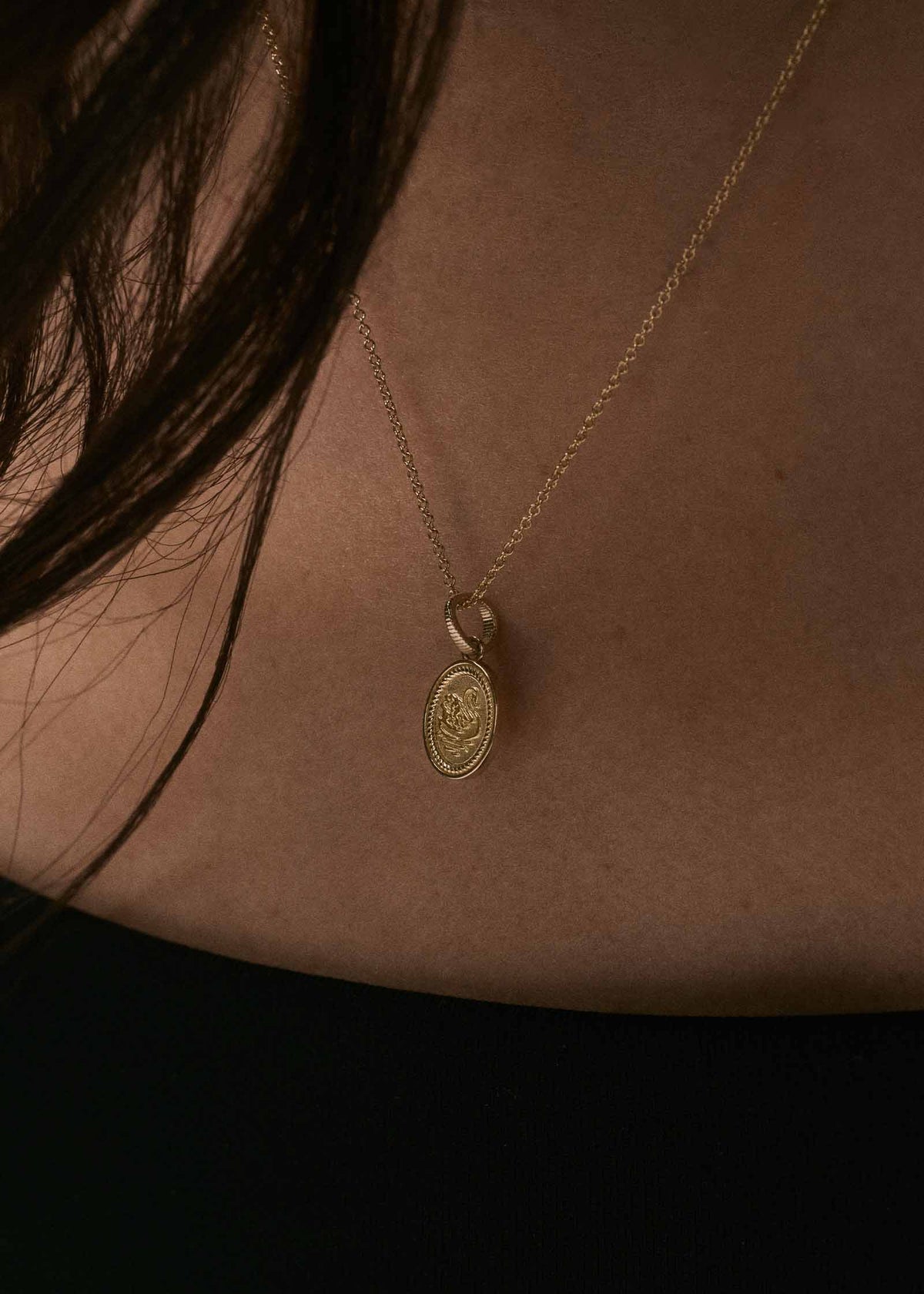 A close-up of a woman in a black top wearing a Kinn Studio 14k Gold Swan Dream Pendant on a Micro Rolo Chain Necklace
