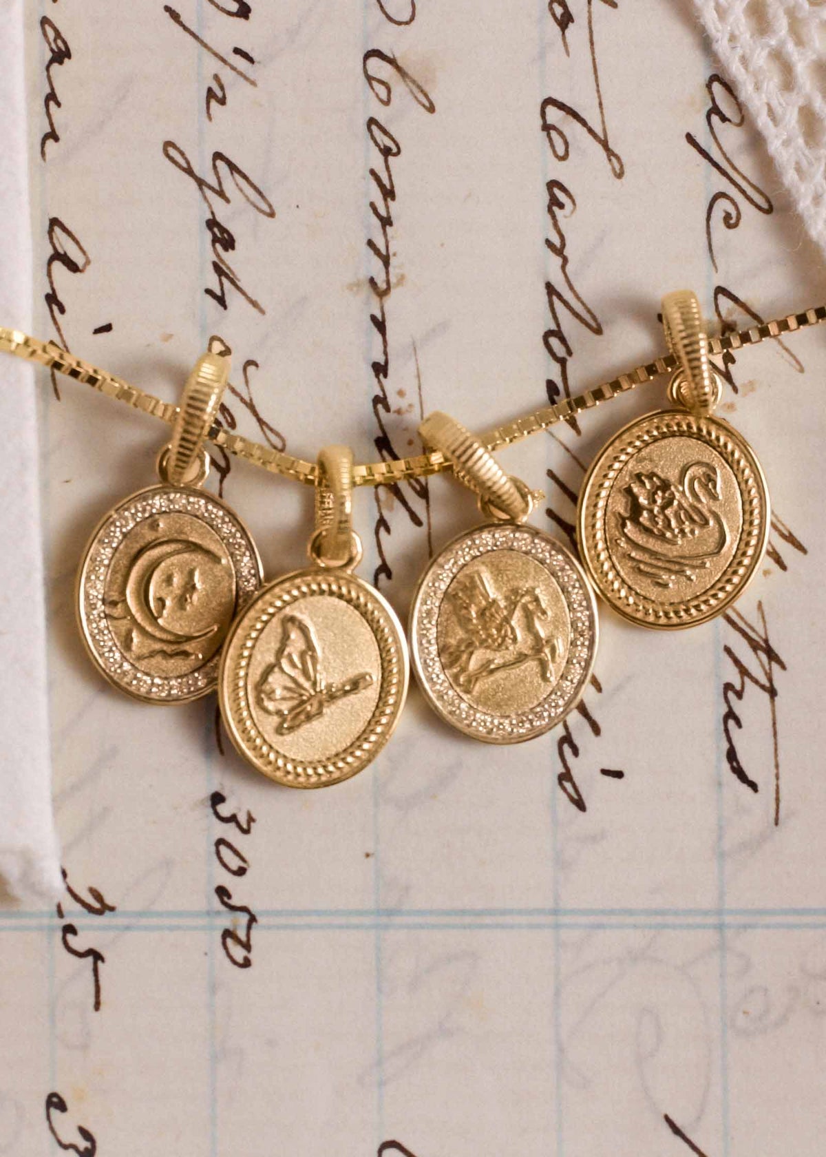 Kinn 14k Gold and Diamond Dream Pendants from the Dare to Dream collection hanging on a box chain necklace draped across a handwritten letter