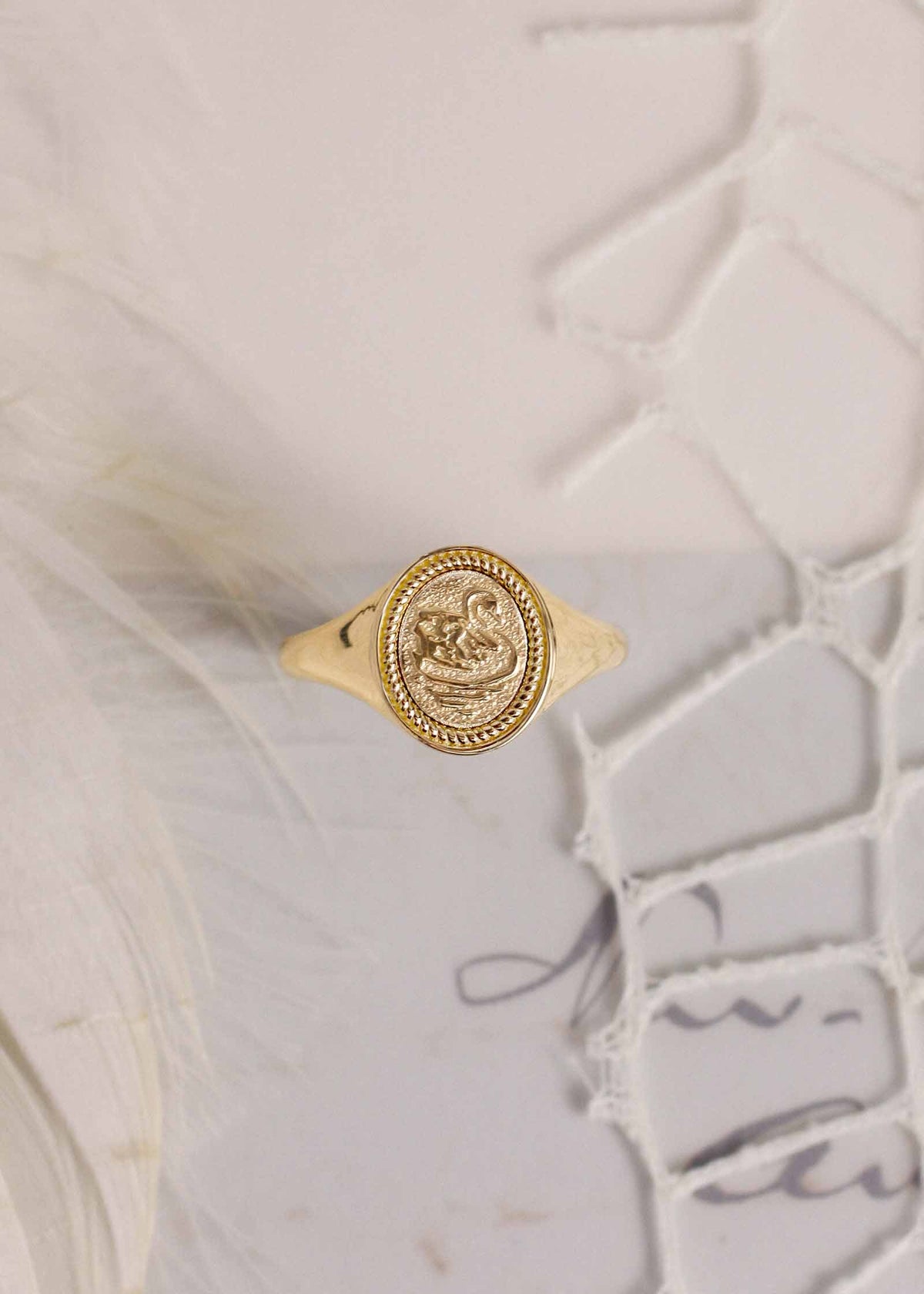 Kinn 14k Gold Swan Dream Signet Ring sitting against a letter, feather and lace