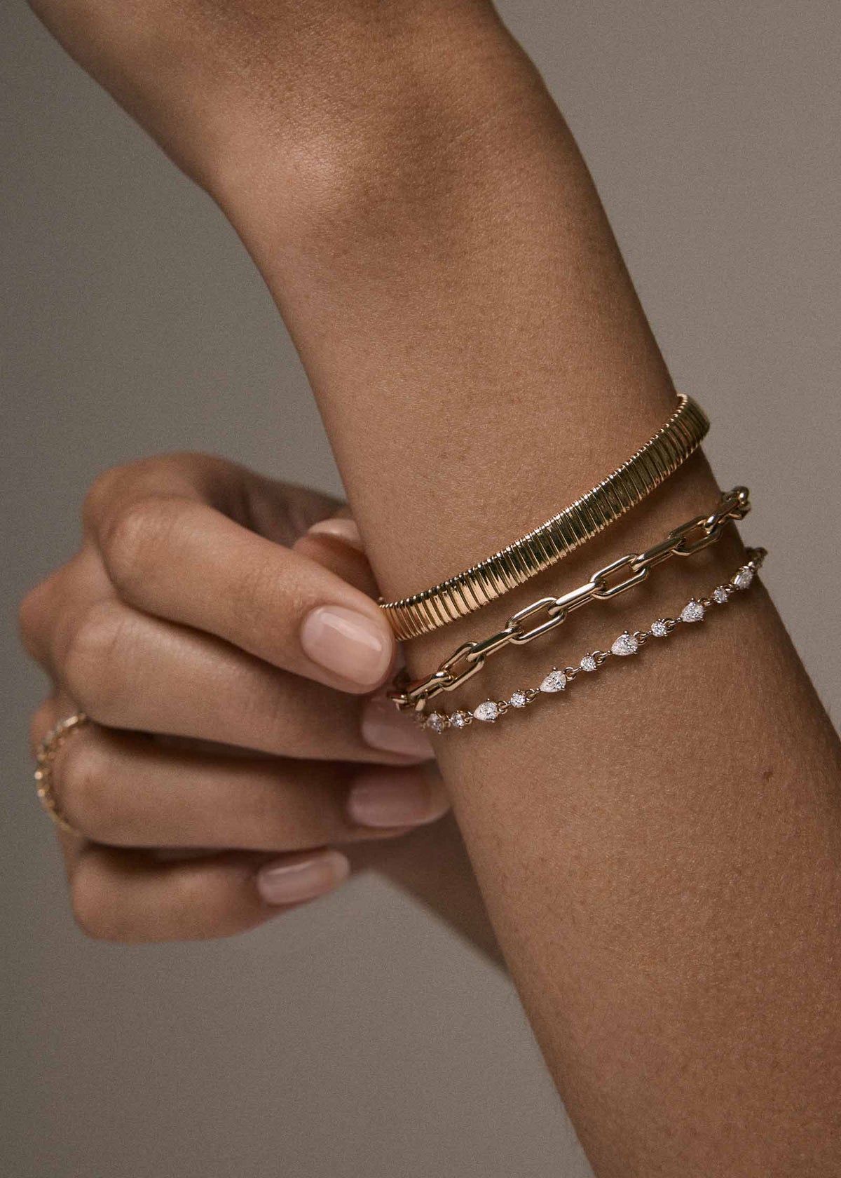 A close-up of a person's wrist wearing a Kinn 14k Gold Celina Flat Tubogas Bracelet stacked with a Mia Link Chain Bracelet and a Juliette Diamond Row Bracelet
