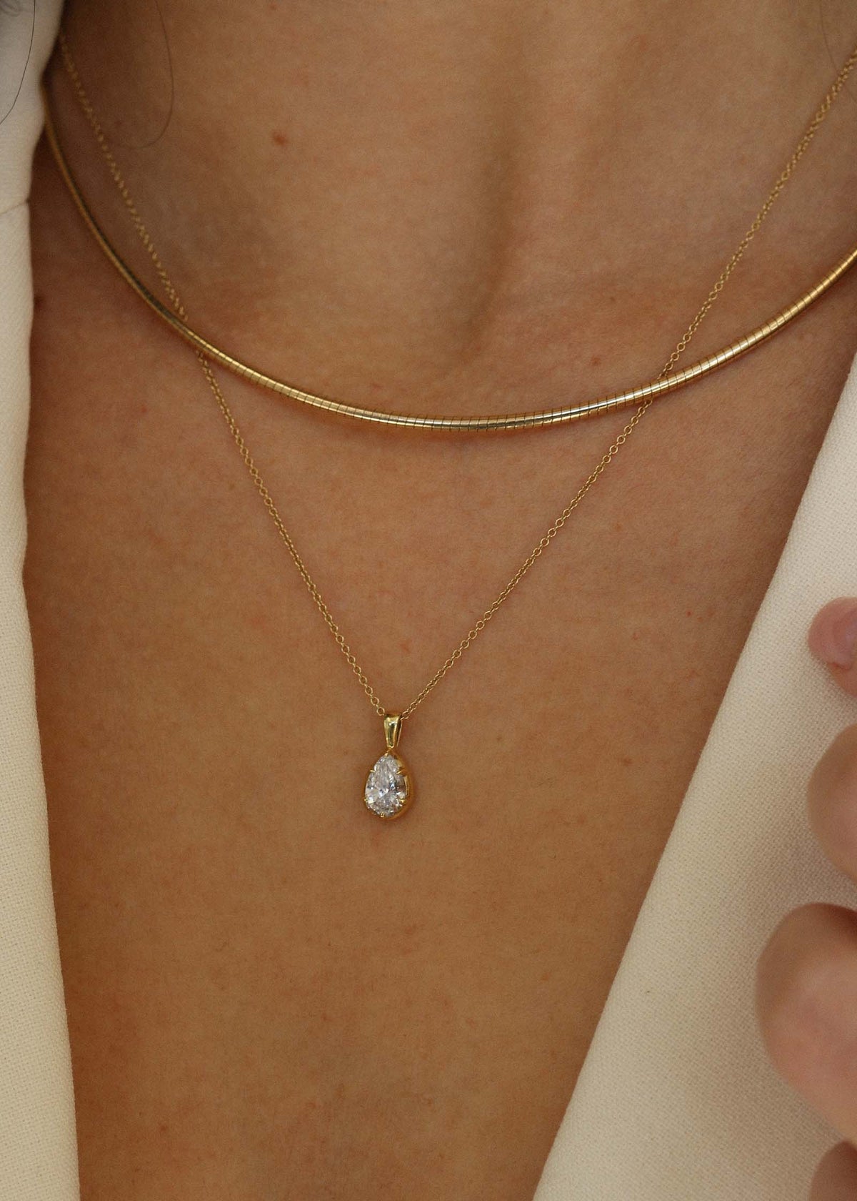 close up of a woman wearing a Kinn 14k Gold Clara Pear Diamond Pendant on a Micro Rolo Chain Necklace layered with an Heirloom Curved Chain Necklace