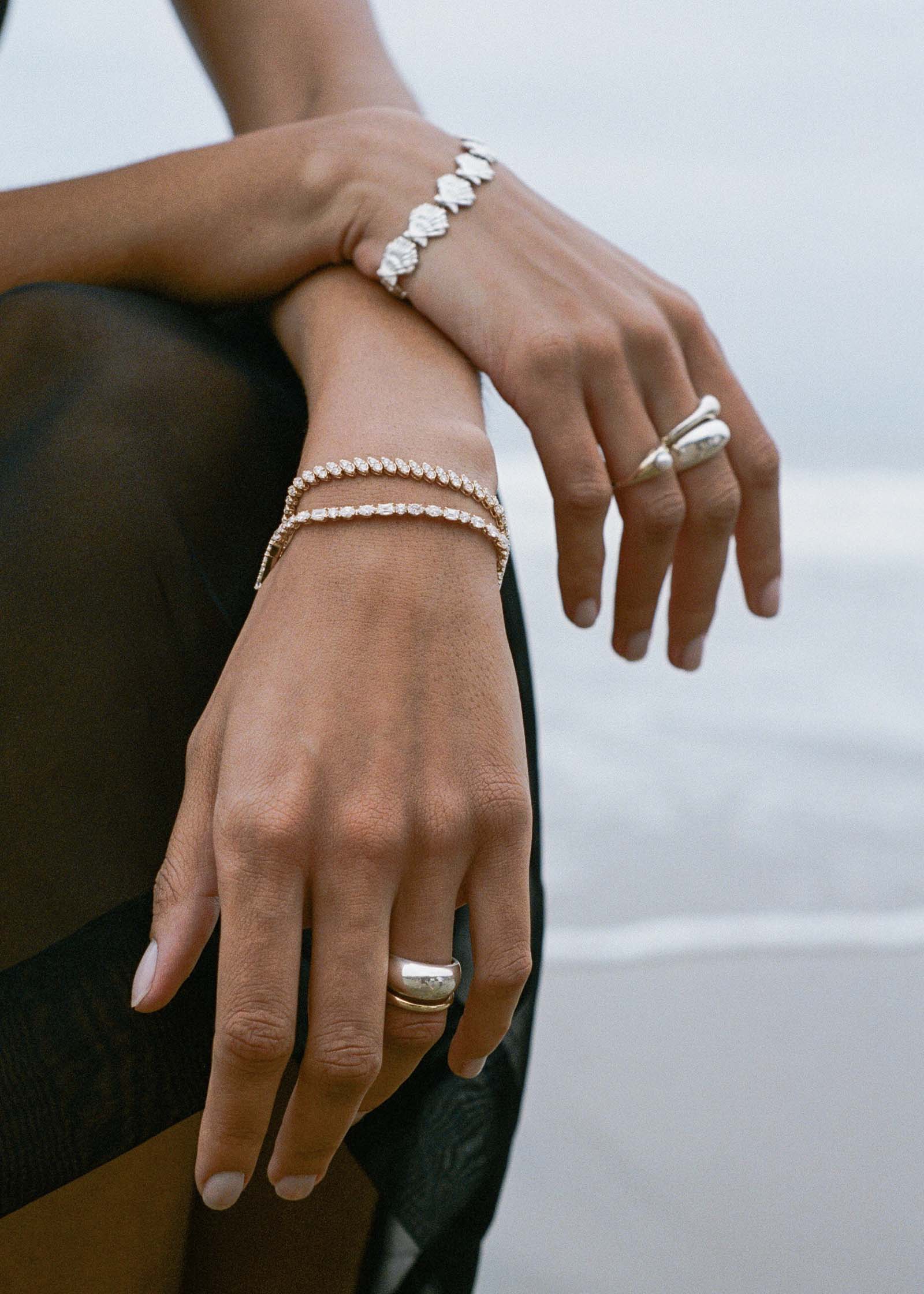 A woman on a beach with her hands crossed wearing a Kinn Studio 14k Gold Esme Fancy Shape Tennis Bracelet stacked with a Sofia bracelet and a Dare to Love Bold Dome Ring in sterling silver