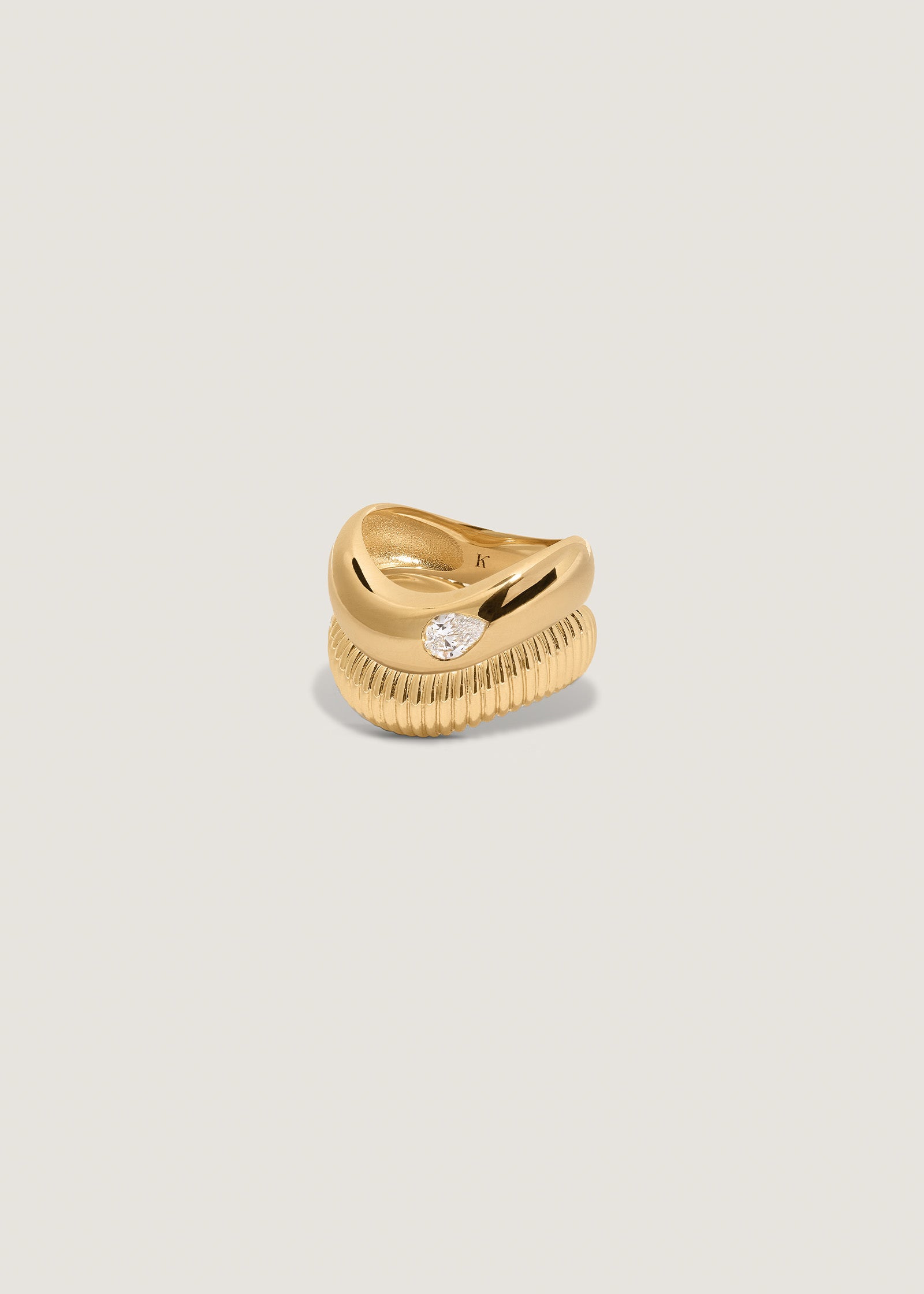 A Kinn 14k Gold Demi Curve Band Ring with a Pear Diamond sitting and a Demi Coil Ribbed Band Ring stacked together
