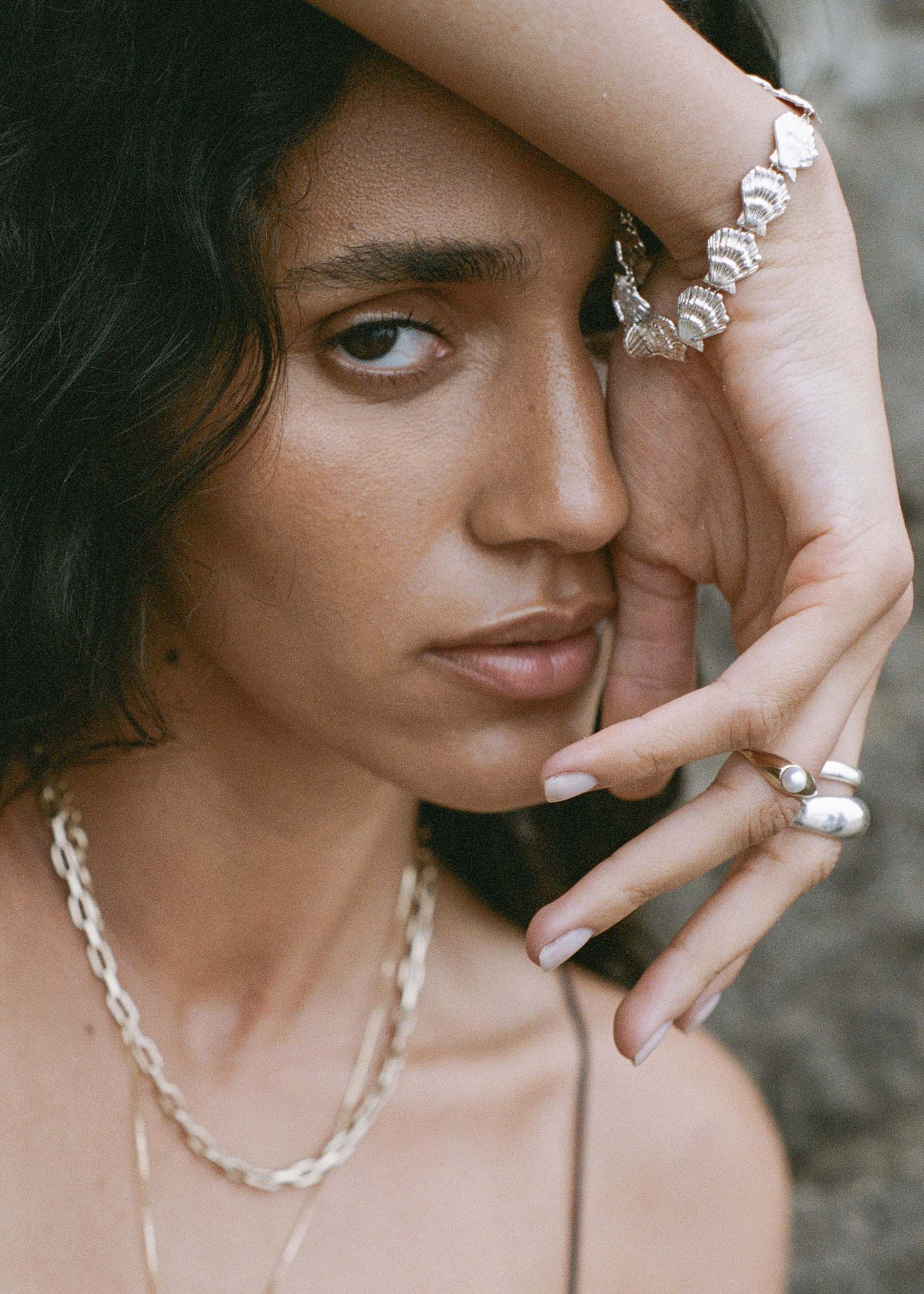 woman with her hand draped over her head wearing a Kinn Studio Sterling Silver Eternity Shell Bracelet on her wrist layered with a Pearl Signet Ring