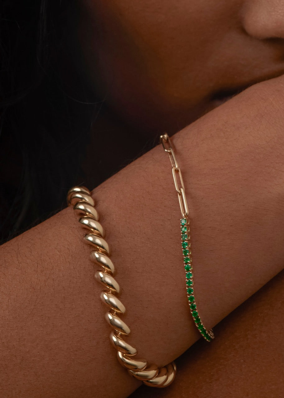 close up of woman's arm wearing a Kinn 14k Gold Coco Round Emerald Tennis Link Bracelet stacked with a Hampshire House Bracelet