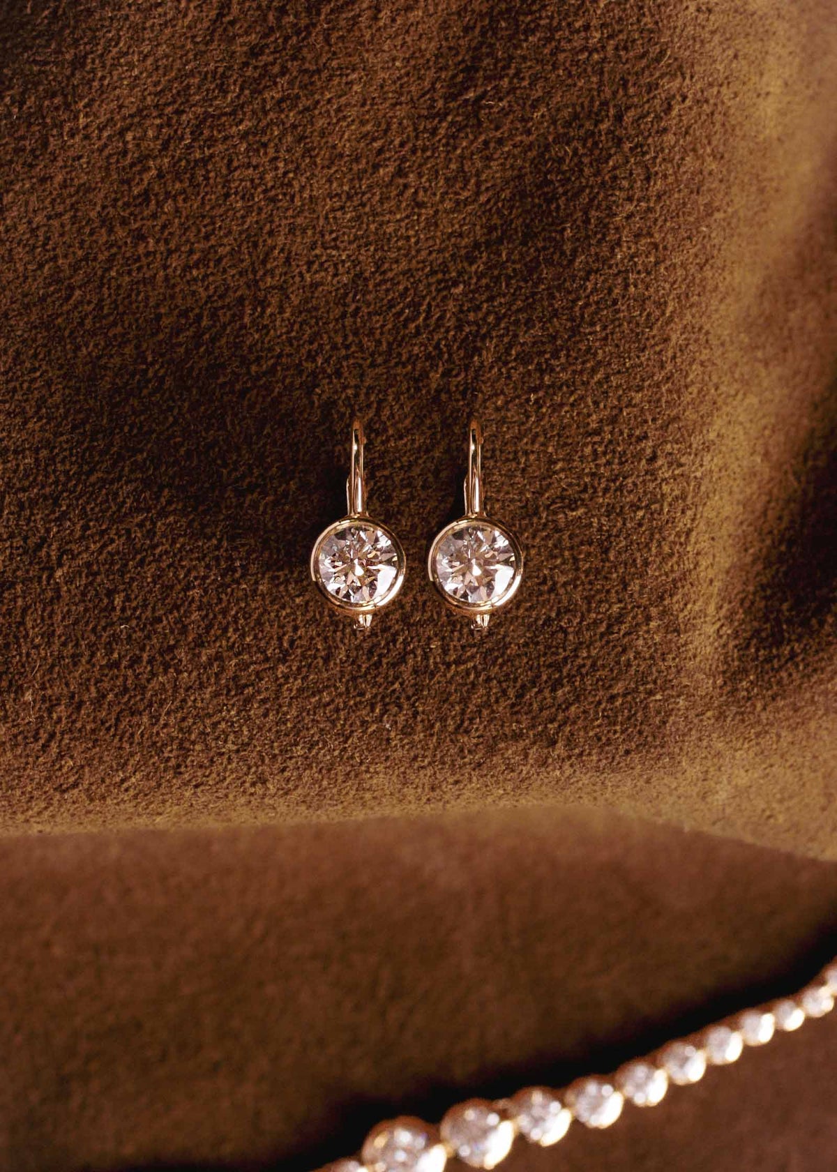 A pair of Kinn 14k Yellow Gold Harper 2ctw Round Drop Earrings laying against a brown suede background
