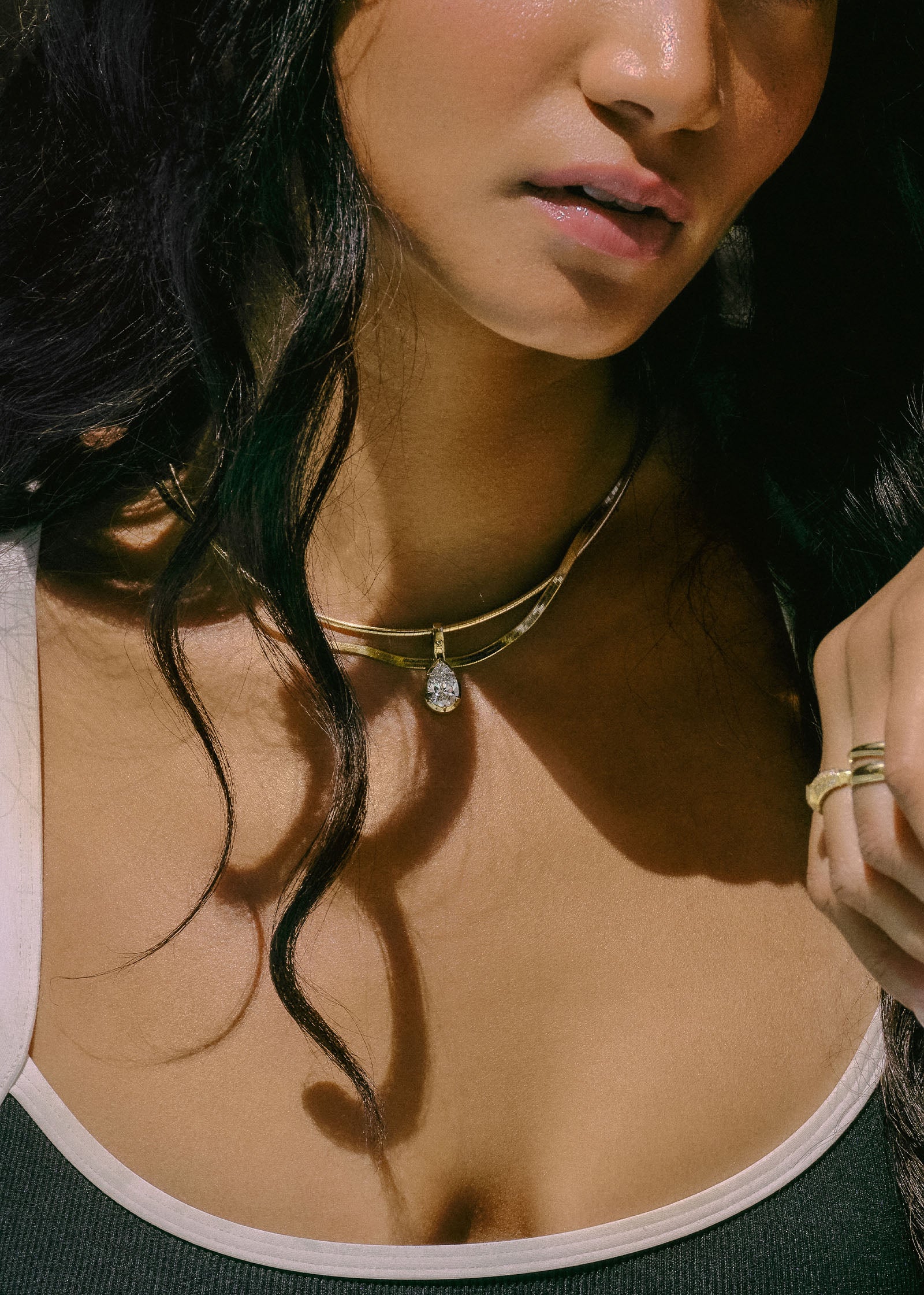 A woman wearing aKinn Studio 14k Gold Heirloom Curved Chain Necklace with a Madeleine Pear Pendant layered with a Carter Herringbone Necklace