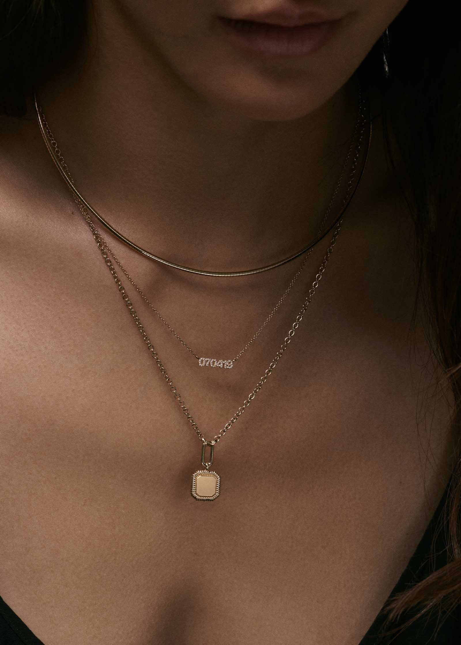 woman wearing a Kinn 14k Gold Oria Ribbed Octagon Pendant Necklace layered with a Heirloom Curved Chain Necklace and a Legacy Pave Diamond Nameplate Necklace customized with a date