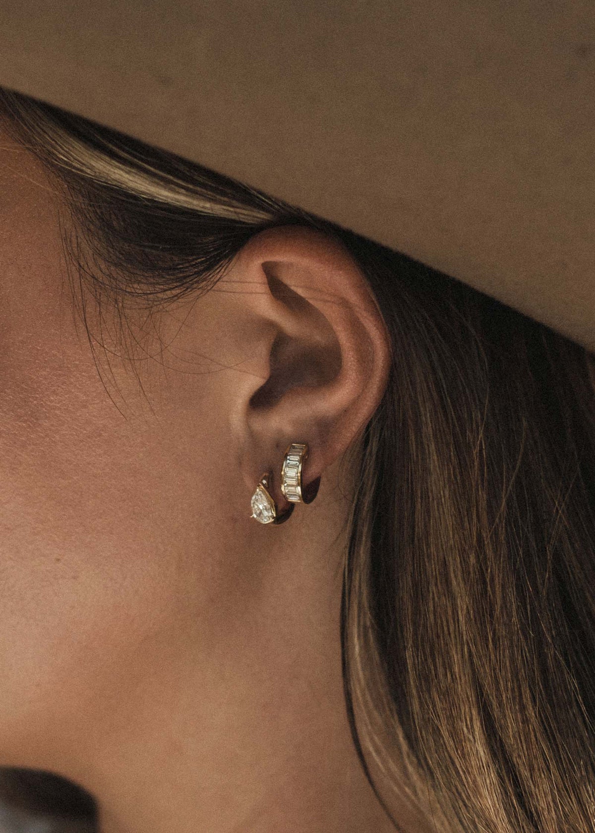 woman wearing Kinn 14k Gold Jackson Pear Diamond Huggie Hoop Earrings layered with Bobbi Baguette Hoops