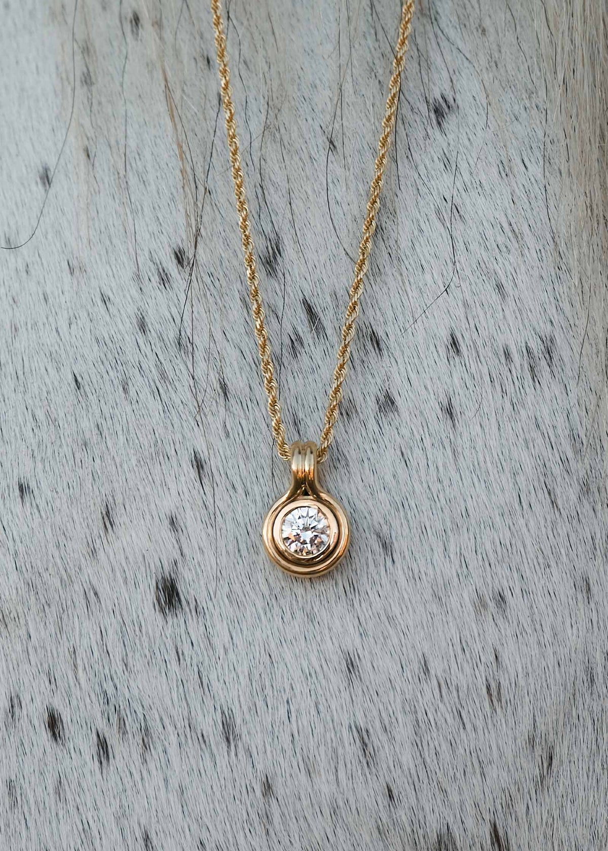 Kinn 14k Gold Jody Round Diamond Pendant Necklace on Rope Chain laying against a speckled white and black horse