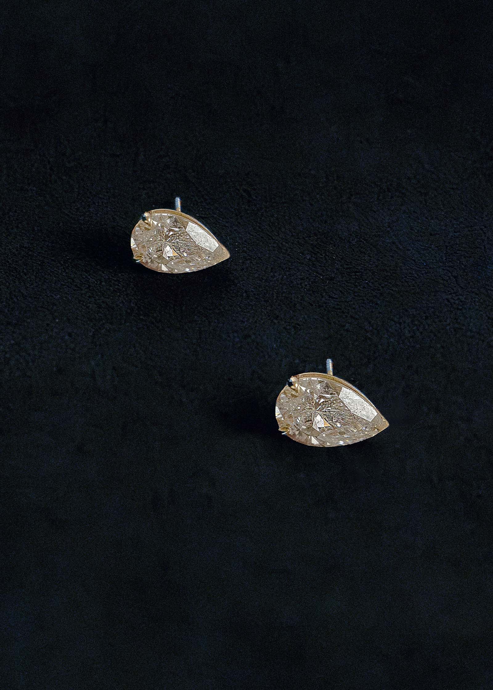A pair of Kinn x Prince 14k Gold June Pear Diamond Stud Earrings laying flat against a dark blue navy velvet background