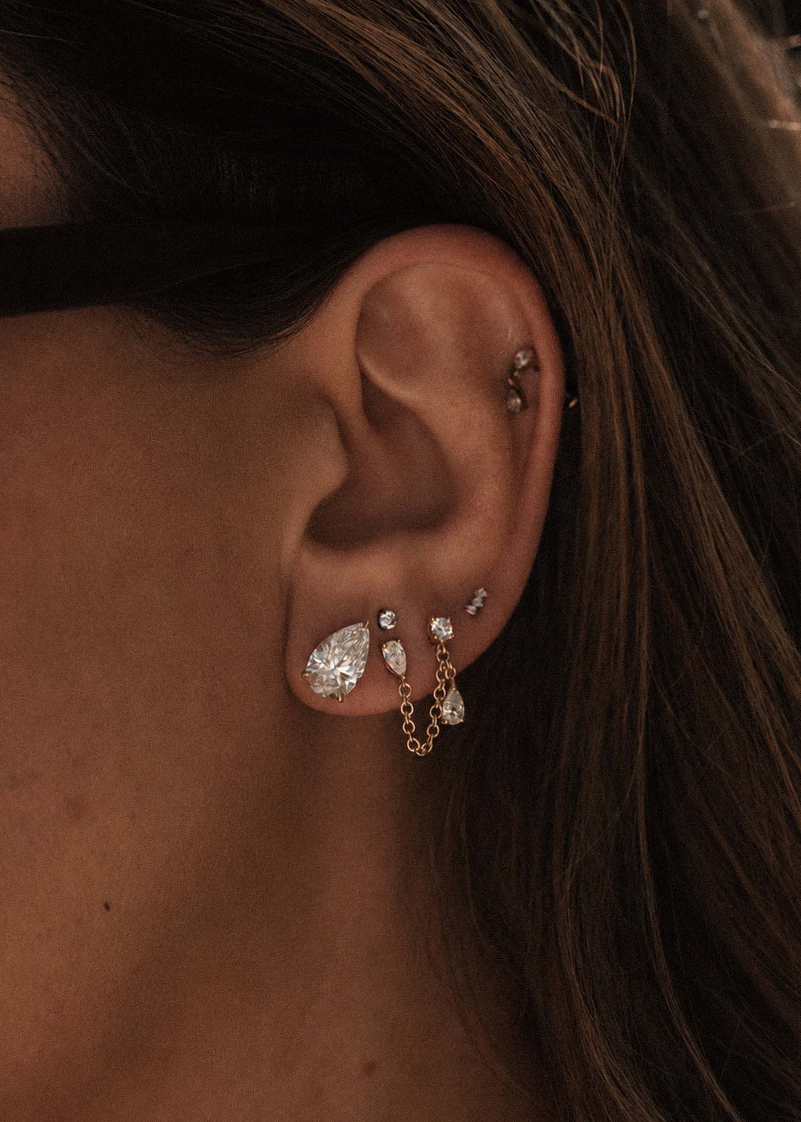 close up of a woman's ear wearing a Kinn x Prince 14k Gold June Pear Diamond Stud Earring layered with a Doubles Diamond Chain Earring