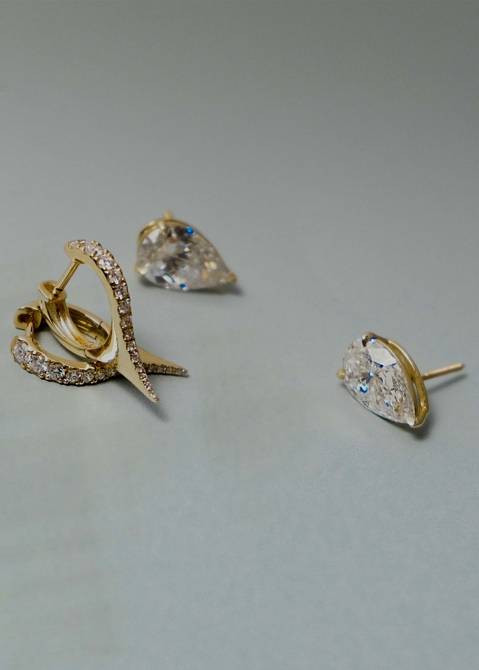 A pair of Kinn x Prince 14k Gold June Pear Diamond Stud Earrings laying flat next to a pair of Point Pave Diamond Huggies