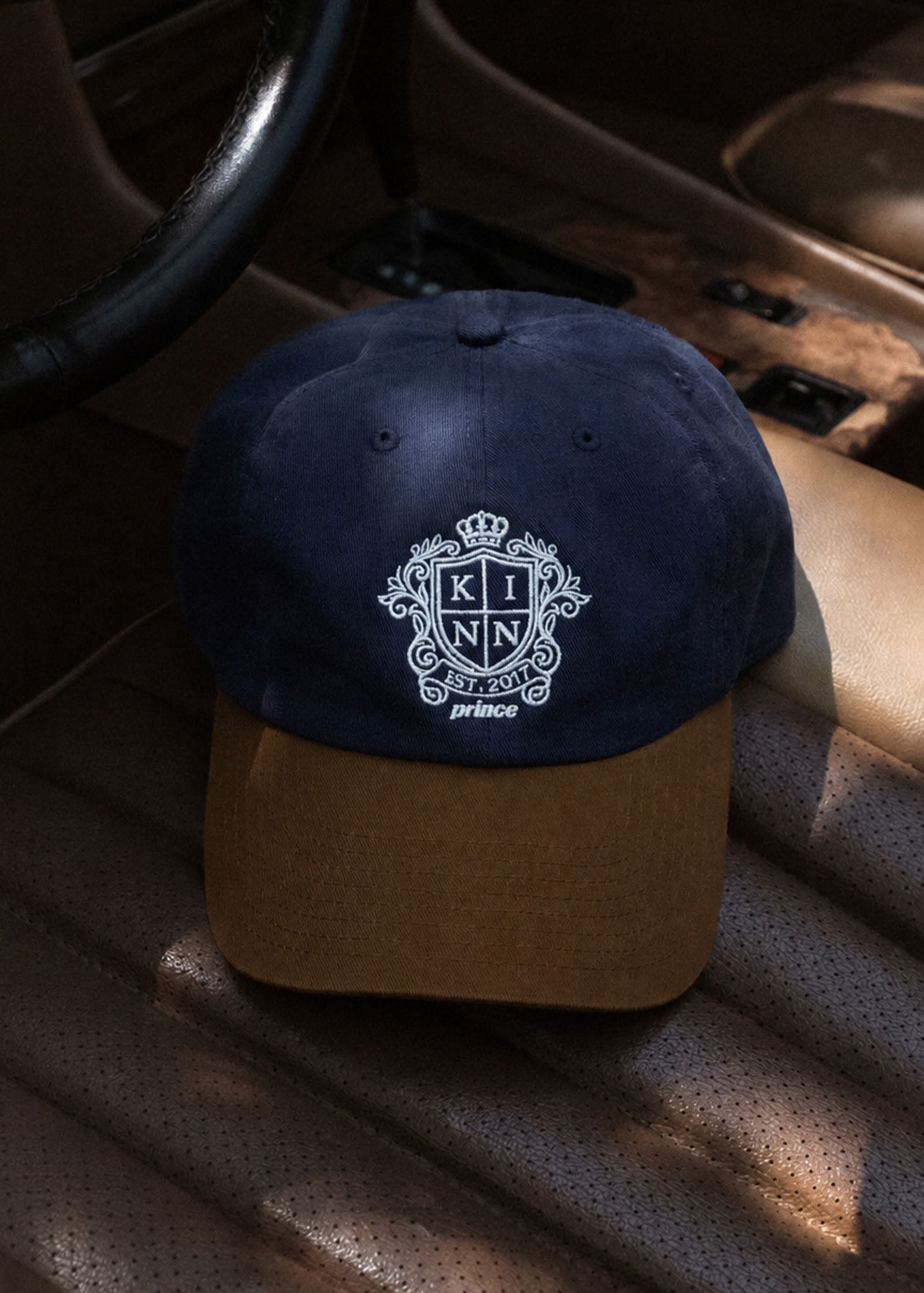 Kinn x Prince The Court Cap laying on a leather seat of a car