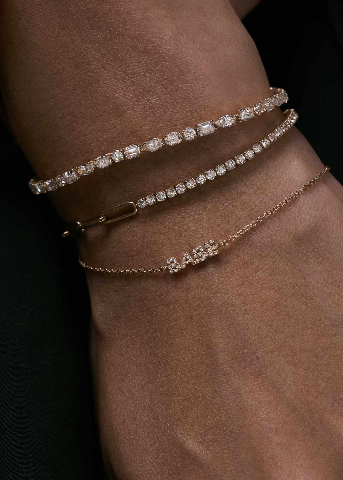 close up of a woman wearing a Kinn Studio 14k Gold Coco Round Diamond Tennis Link Bracelet stacked with an Esme DIamond Tennis Bracelet and Legacy Nameplate Bracelet reading "Babe"