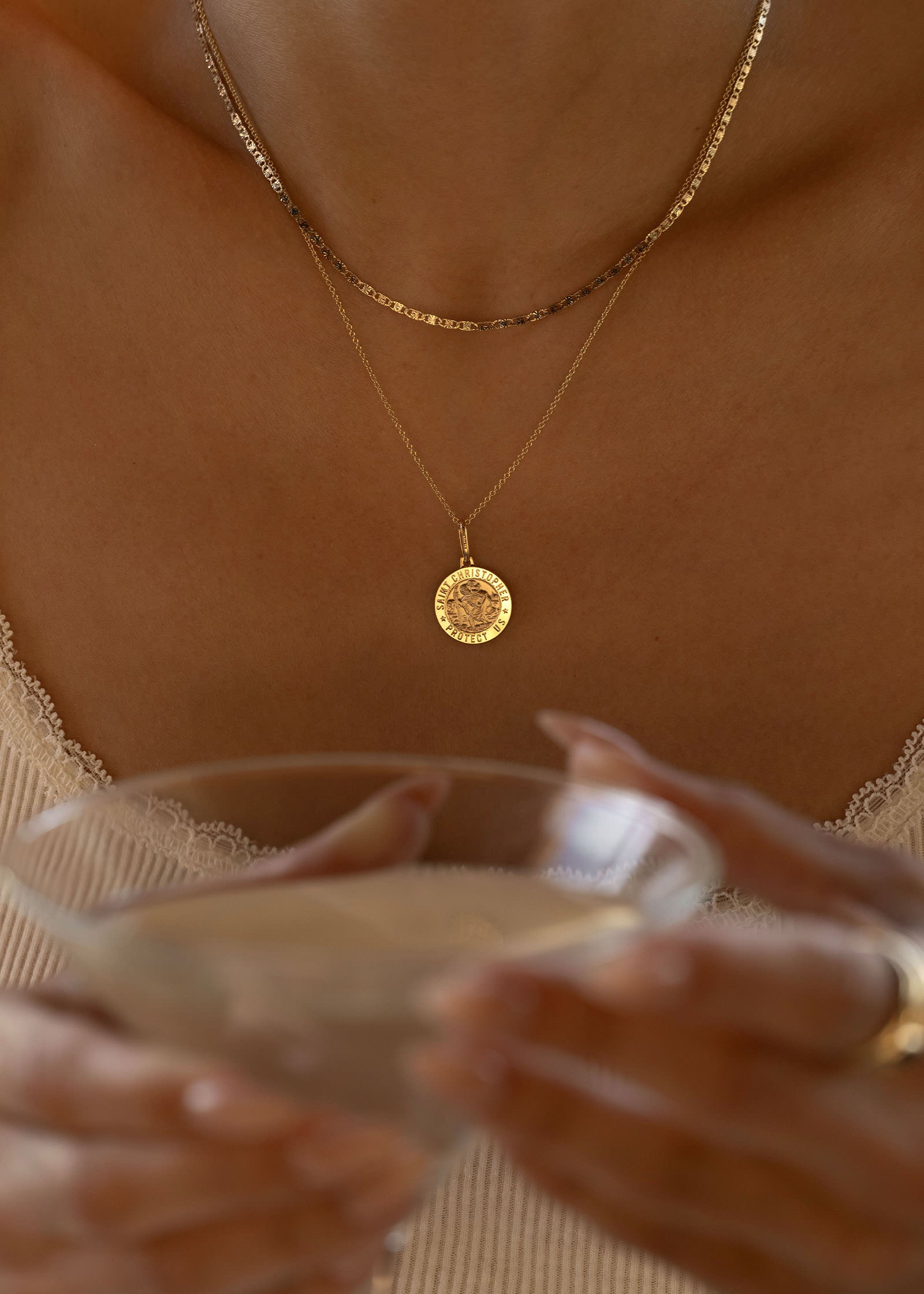 woman holding a martini glass wearing a Kinn 14k Gold Saint Christopher Charm Pendant on a Micro Rolo Chain Necklace layered with a Valentino Tri Color Gold Chain