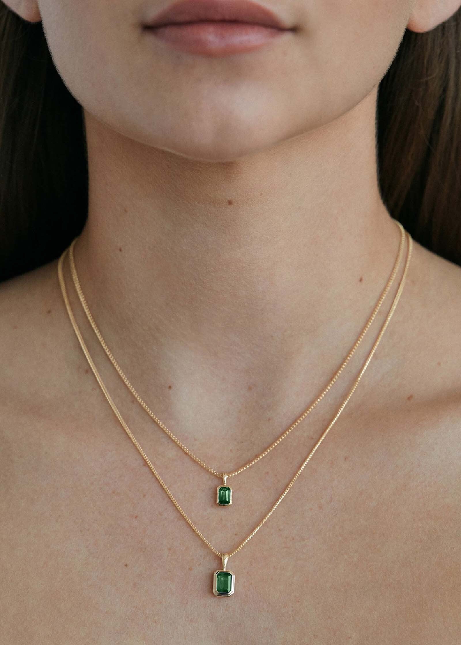woman wearing a Kinn 14k Gold Lyra Emerald Cut Emerald Pendant on a chain necklace layered with a Brooklyn Emerald Cut Emerald Pendant Necklace