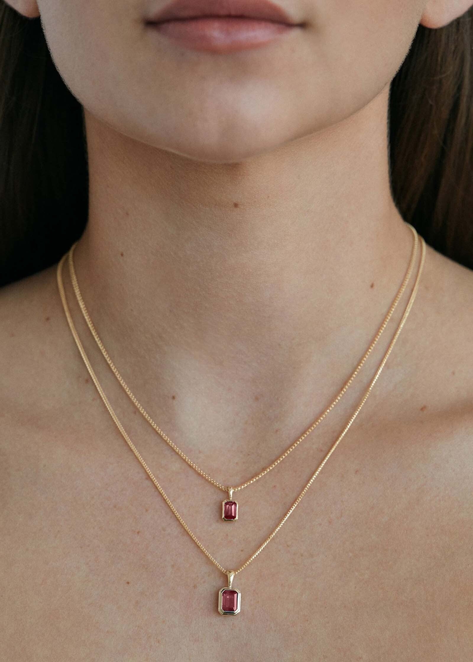 woman wearing a Kinn 14k Gold Lyra Emerald Cut Ruby Pendant on a chain necklace layered with a Brooklyn Ruby Pendant on a chain