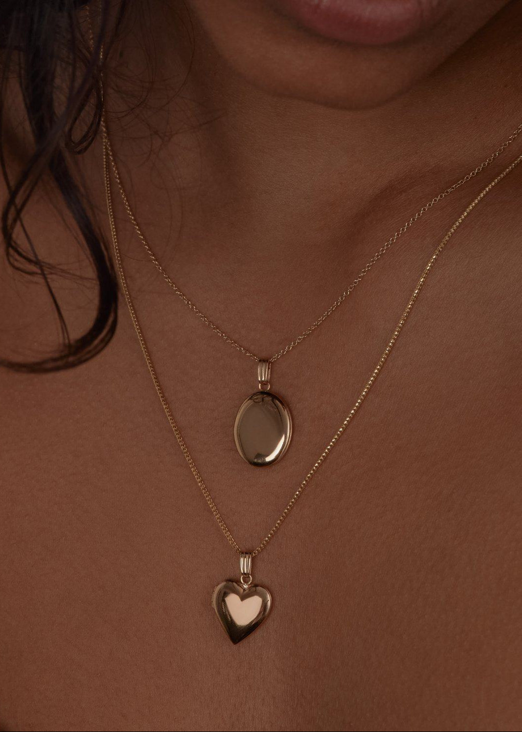 woman wearing a Kinn 14k Gold Maison Oval Locket Necklace layered with a Maison Heart Locket Necklace