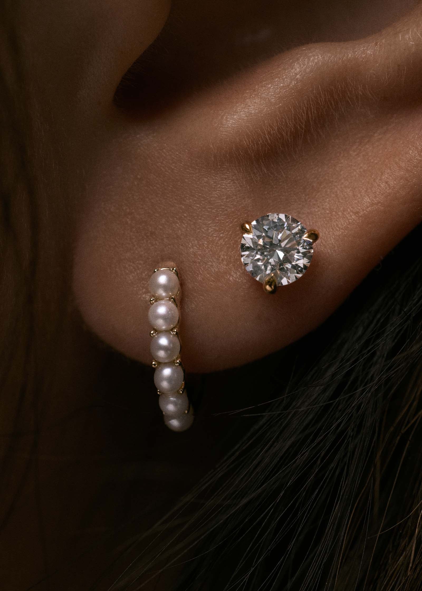 close up of an ear wearing a Kinn 14k Gold Marina Pearl Huggie Hoop Earring with a June Round Diamond Stud