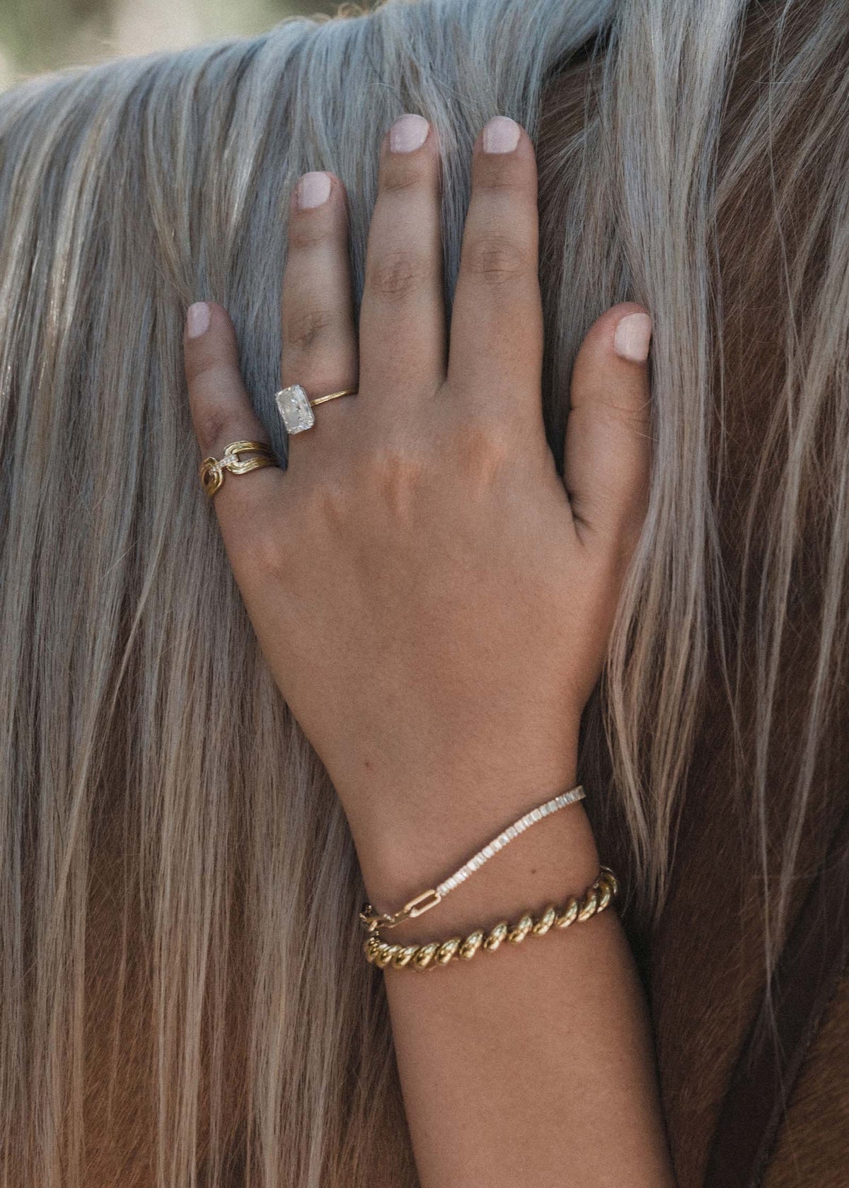 A woman's hand against a horse's mane wearing a Kinn 14k Gold Nicky Double Horseshoe Ring on her pinky and a Serena Baguette and Hampshire House Bracelet on her wrist