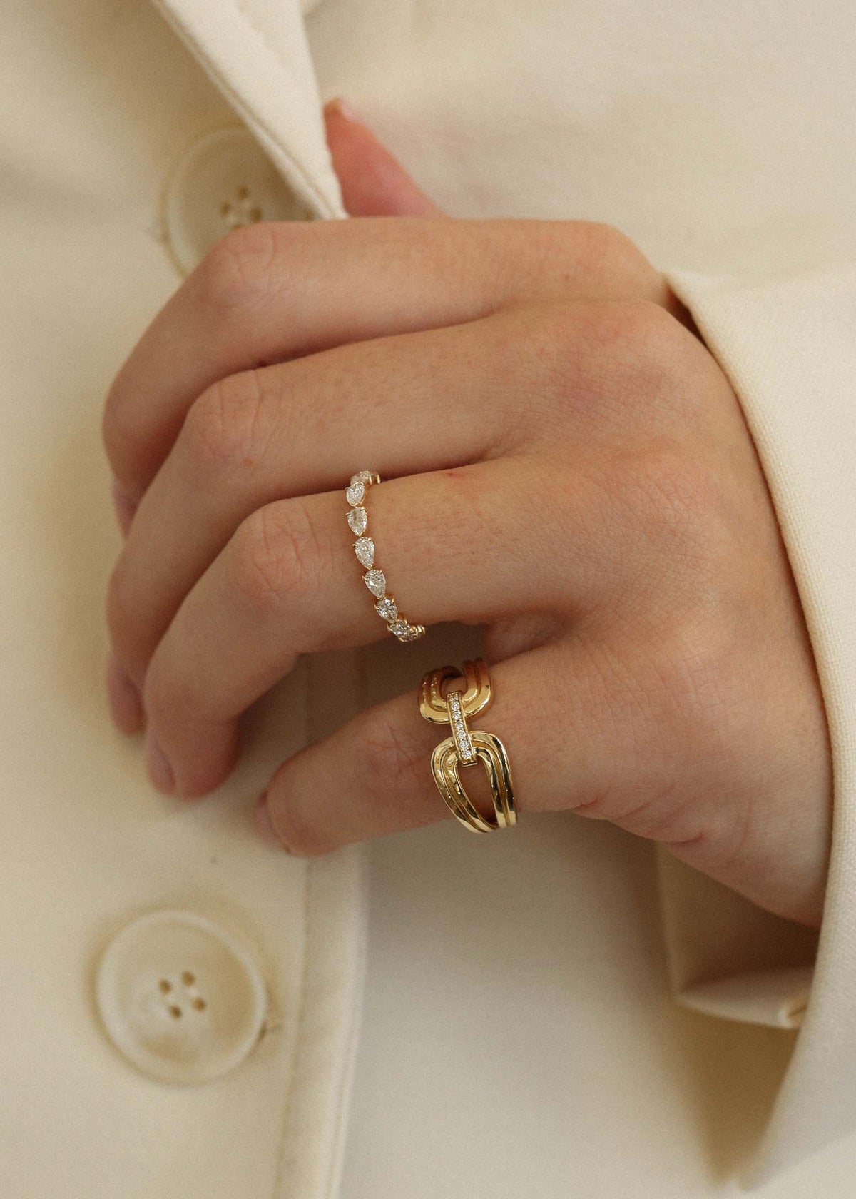 close up of woman's hand wearing a Kinn 14k Gold Nicky Double Horseshoe Ring on her pinky and a Petite Pear Diamond Eternity Band Ring on her ring finger