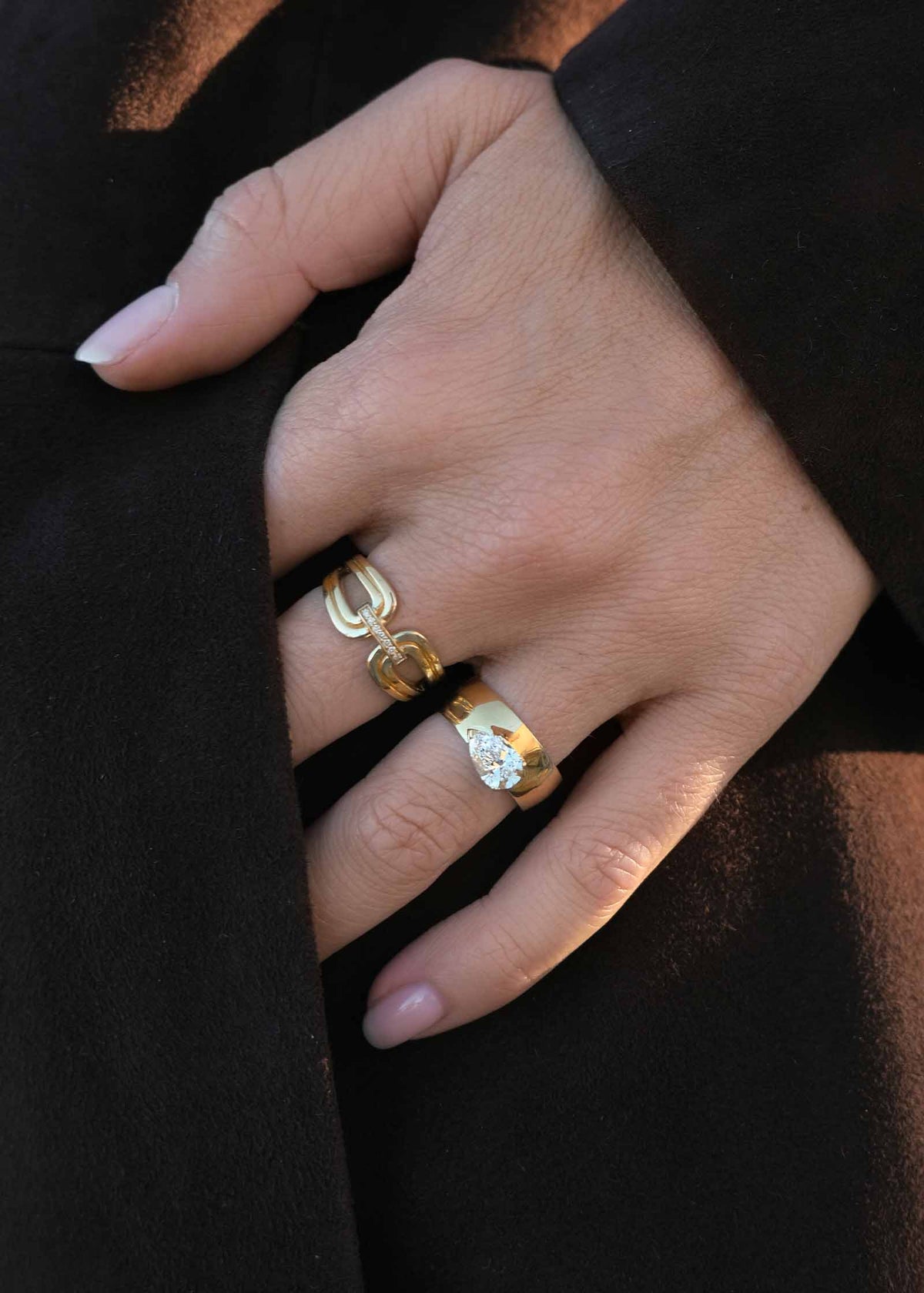 A woman's hand in her pocket wearing a Kinn 14k Gold Nicky Double Horseshoe Ring and a Porter Cigar Band Pear Diamond Ring