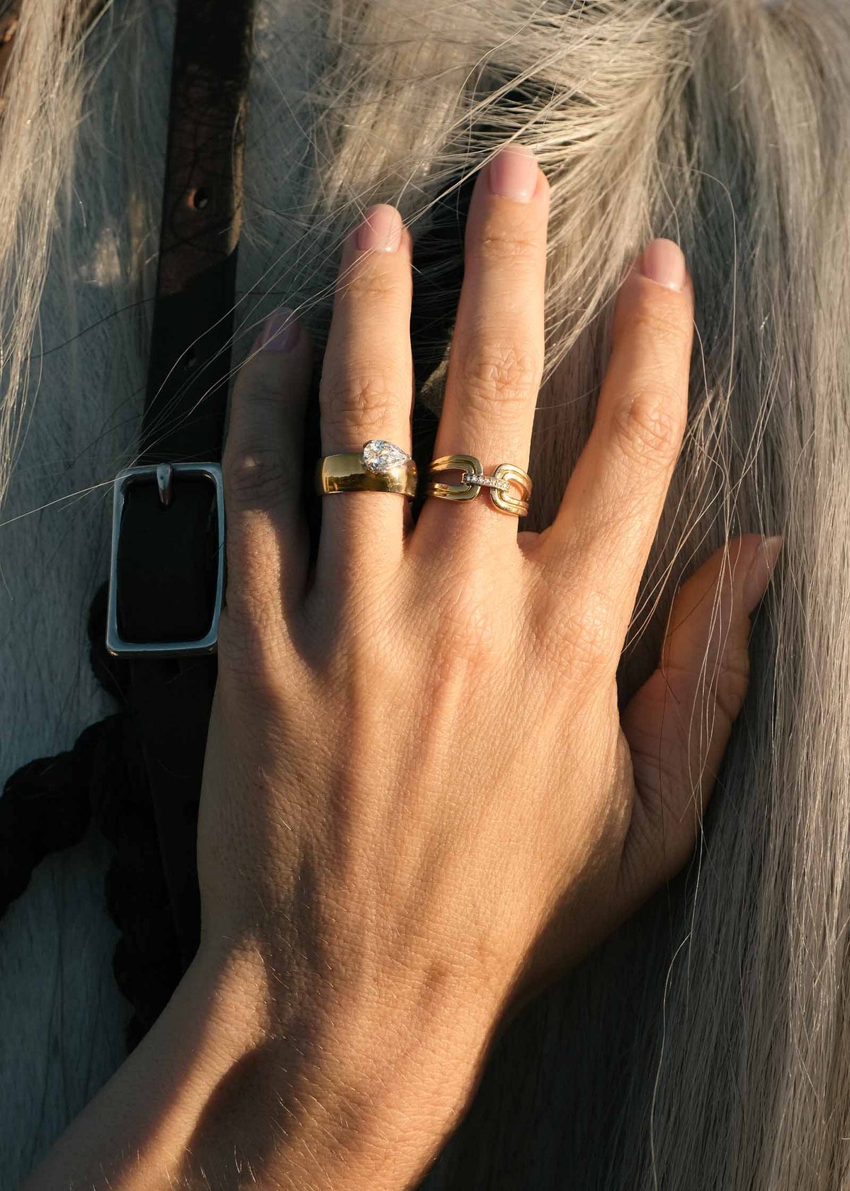 A Kinn 14k Gold Nicky Double Horseshoe Ring and Porter Cigar Band Pear Diamond Ring on a woman's hand against a white horse's mane