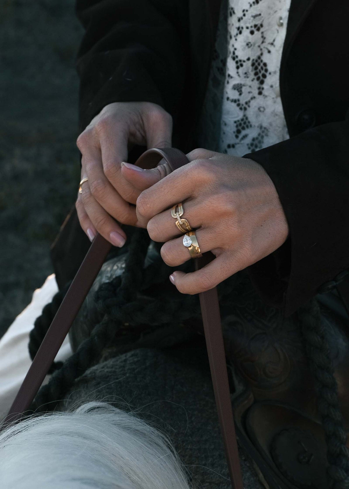 A woman riding a horse and holding the reins while wearing a Kinn 14k Gold Nicky Double Horseshoe Ring and Porter Cigar Band Pear Diamond Ring