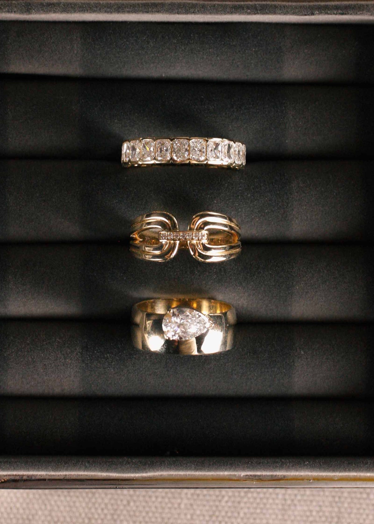 A Kinn 14k Gold Nicky Double Horseshoe Ring, Jane Radiant Diamond Eternity Ring, and a Porter Cigar Band Pear Diamond Ring sitting upright in a jewelry box