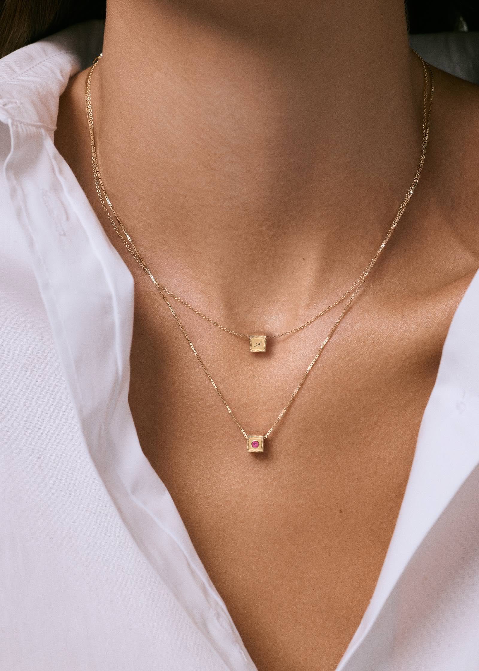 woman in a white shirt wearing two Kinn 14k Gold Chapter Custom Pink Tourmaline Birthstone Charm Necklace with one showing the engraved initial and the other showing the birthstone