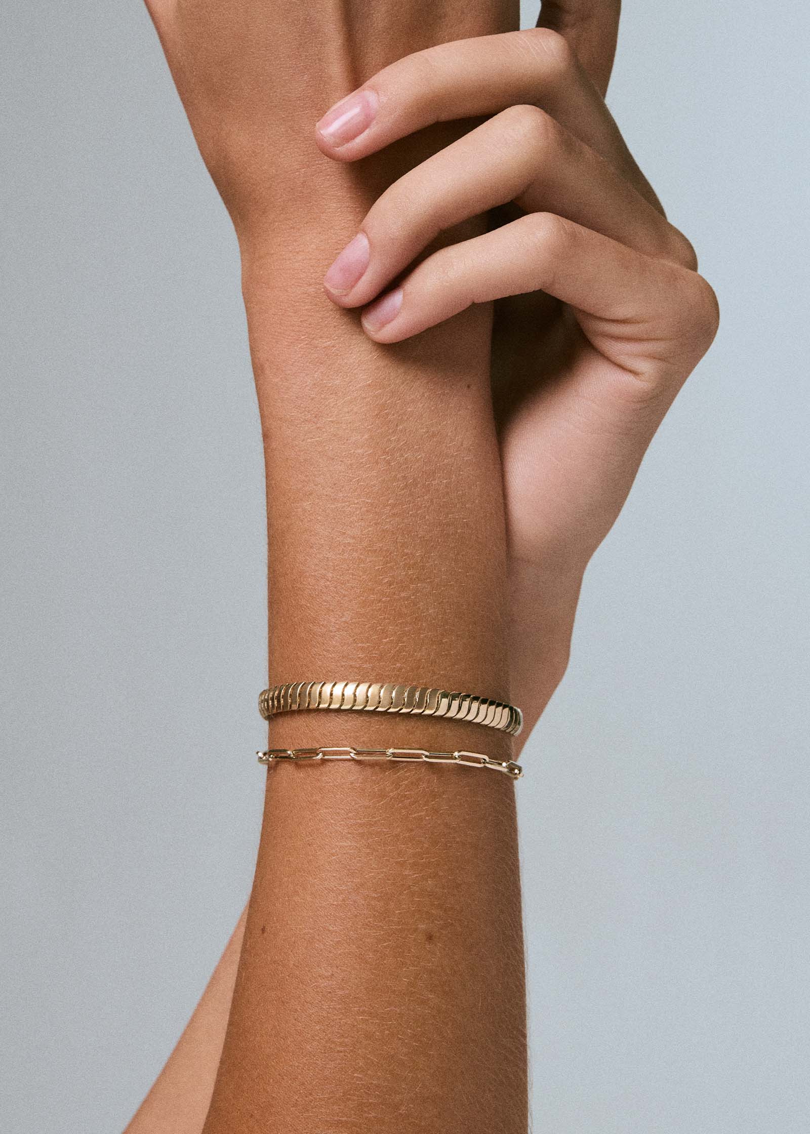 A woman's arm wearing a Kinn 14k Gold Cobra Chain & Paperclip Link Chain Bracelet stack