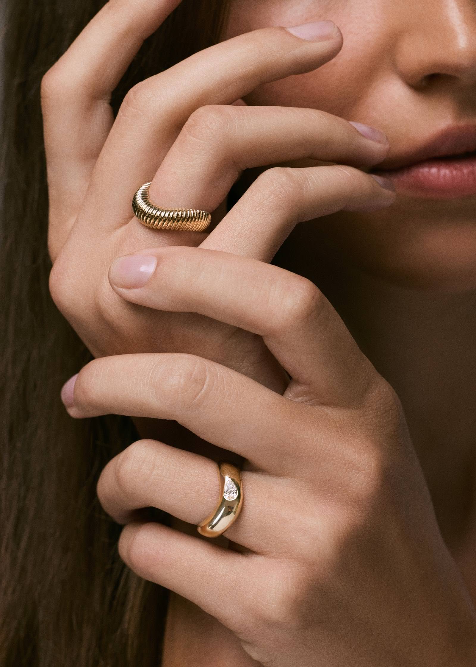 A Kinn 14k Gold Demi Curve Band Ring with a Pear Diamond on a woman's left ring finger and a Demi Coil Ribbed Band Ring sitting on her right ring finger