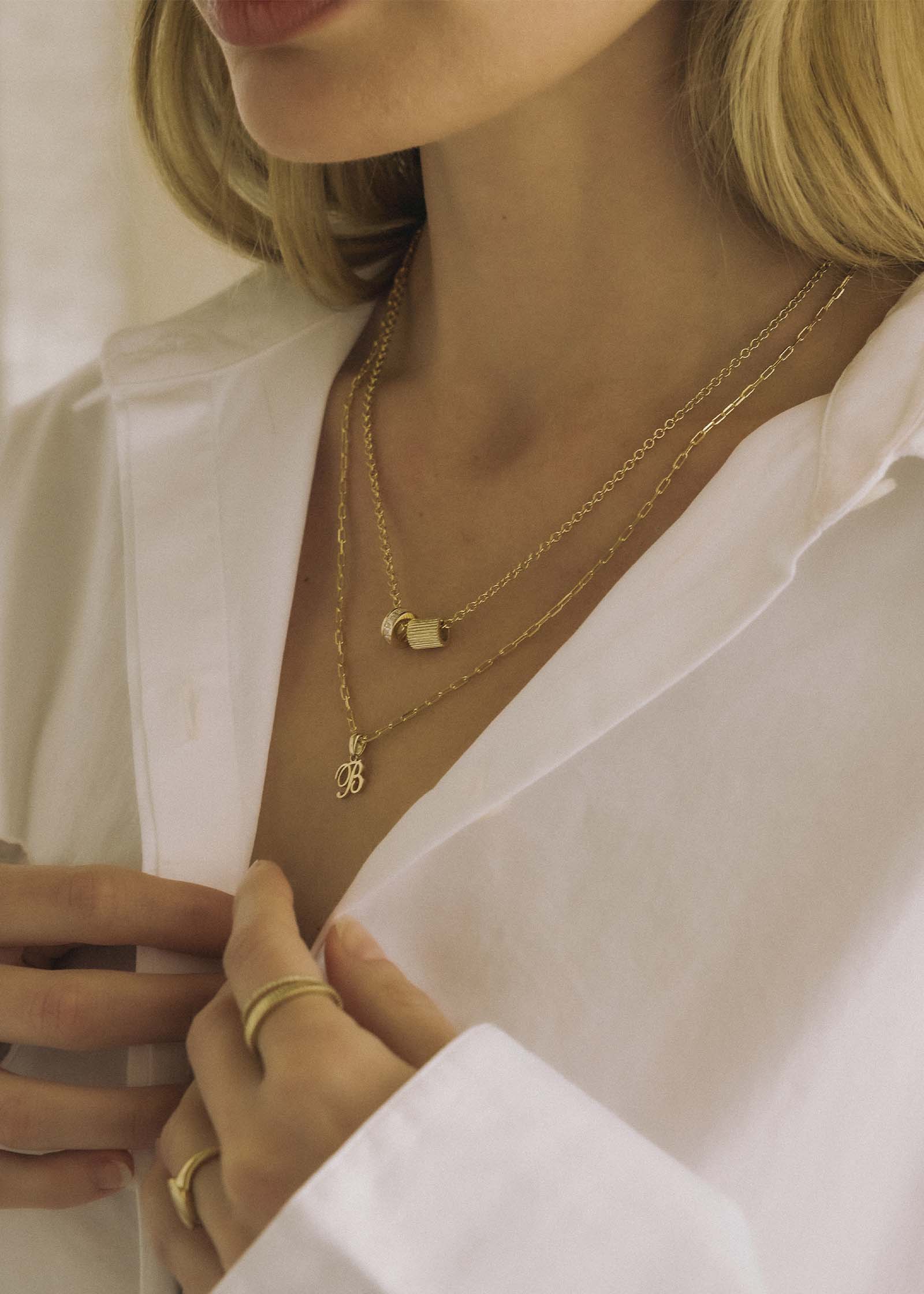 woman in a white shirt wearing a Kinn x Shoppe Amber Interiors The Estate Charm 14k Yellow Gold on a cable rolo chain with a diamond charm layered with a Love Letter Pendant Necklace