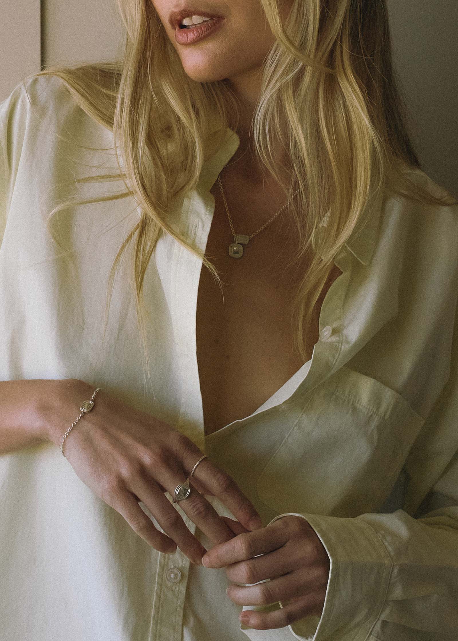 woman in a white button down shirt wearing a Kinn x Shoppe Amber Interiors The Estate Bracelet Sterling Silver along with The Estate SIgnet Ring and Estate Pendant Necklace