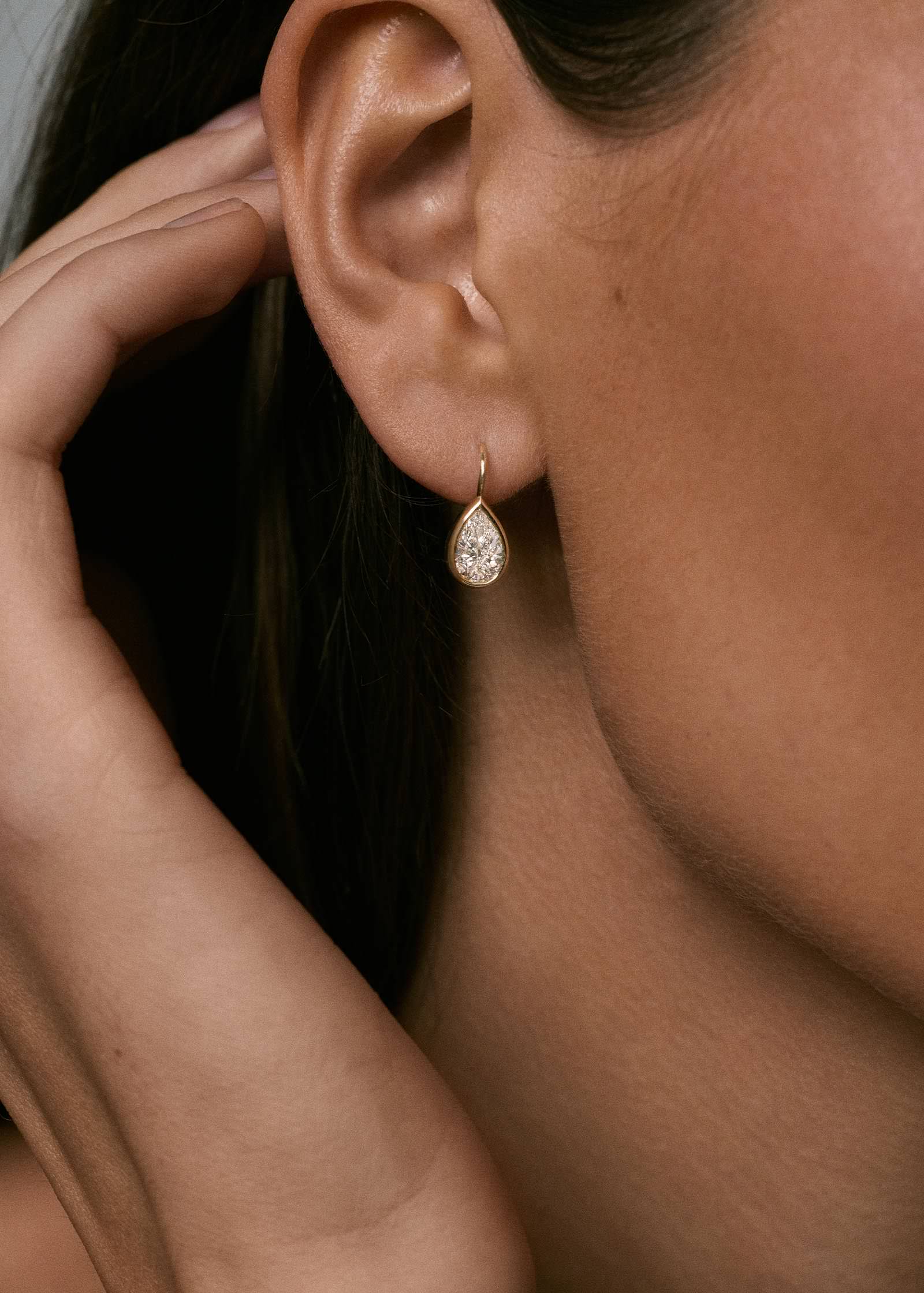 A brunette woman wearing a pair of Kinn 14k Gold 2ctw Pear Diamond Drop Earrings