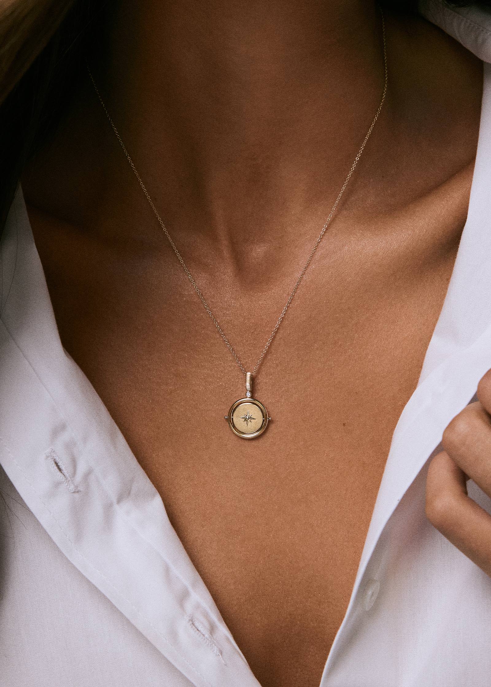 A woman in a white shirt wearing a Kinn 14k Gold Round North Star Birthstone Diamond Pendant Necklace