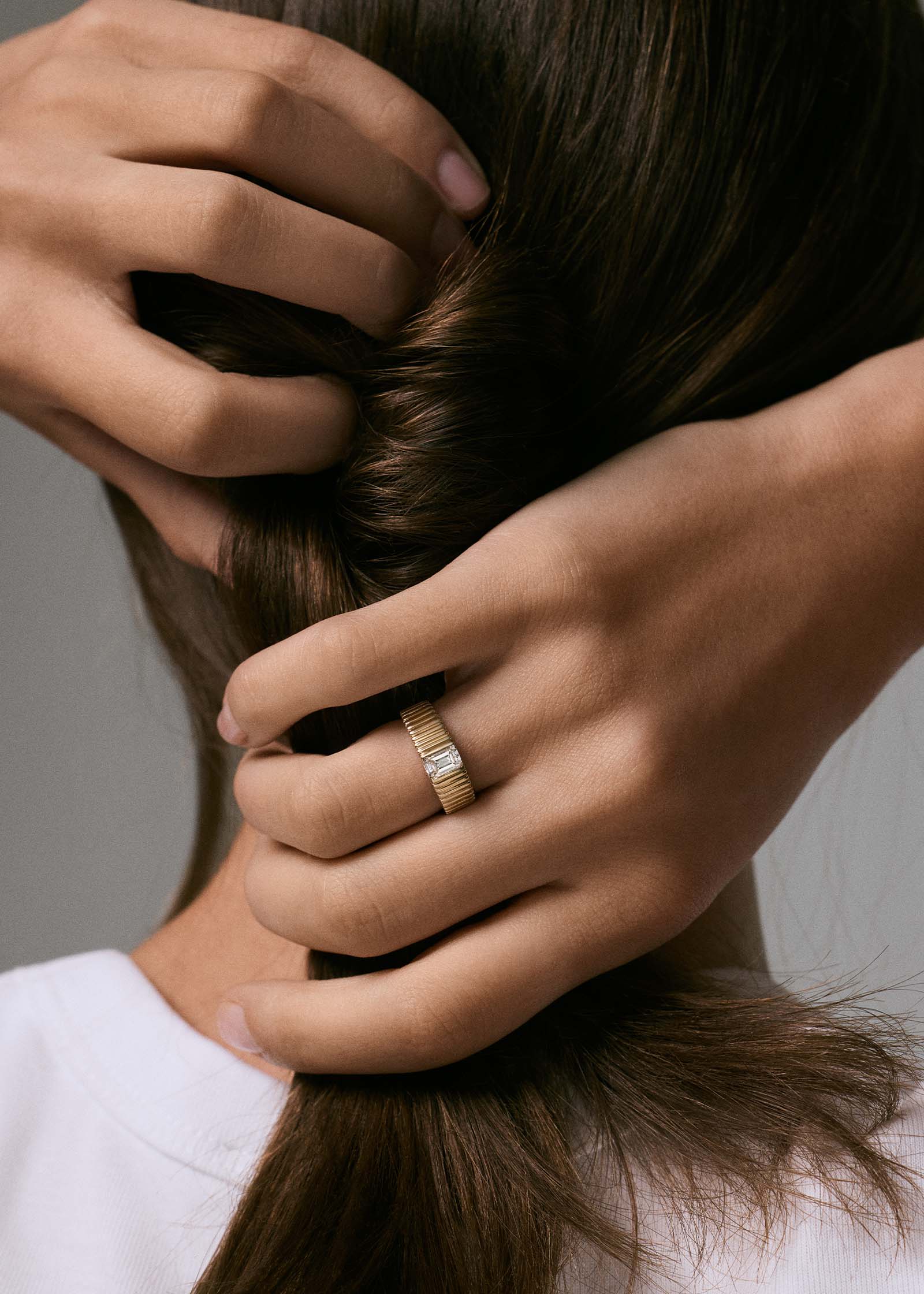 close up of a woman wearing a Kinn 14k Gold Solis Ribbed Ring Emerald Cut Diamond on her ring finger while holding her hair behind the back of her head