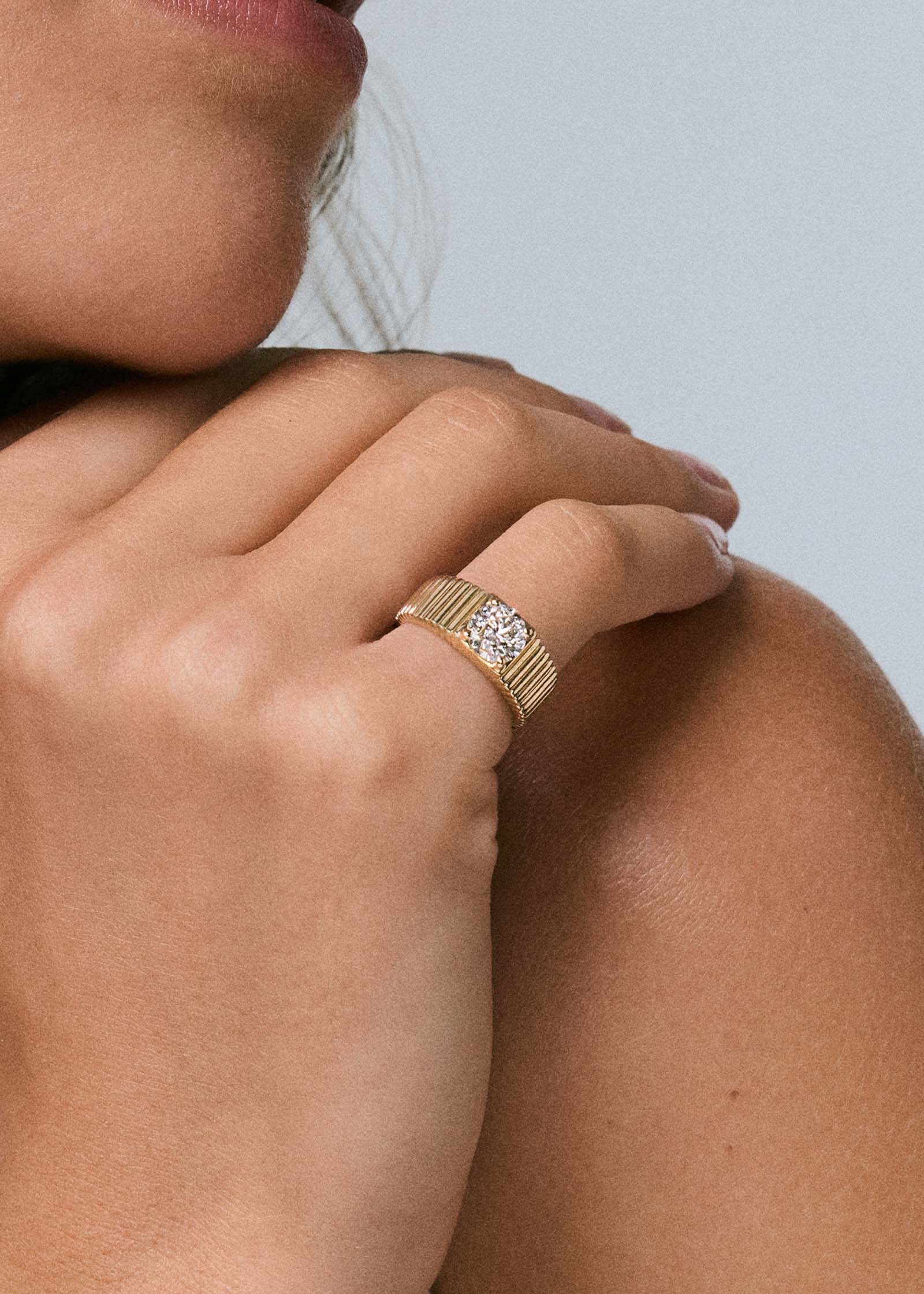 woman's hand resting on her shoulder wearing a Kinn 14k Gold Solis 1.0 Carat Round Diamond Ribbed Band Engagement Ring