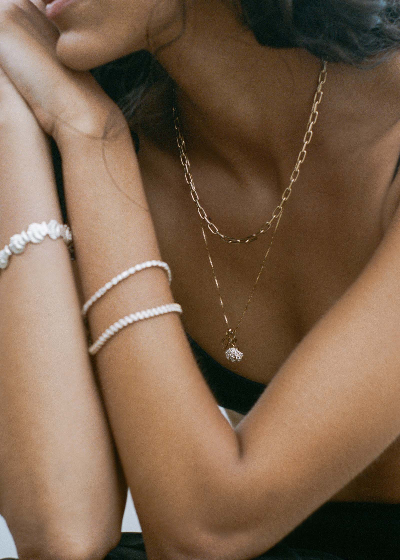 woman on the beach wearing a woman wearing a Kinn 14k Gold Pavé Diamond Shell Charm Necklace on a long box chain and layered with a Mia Link Chain Necklace