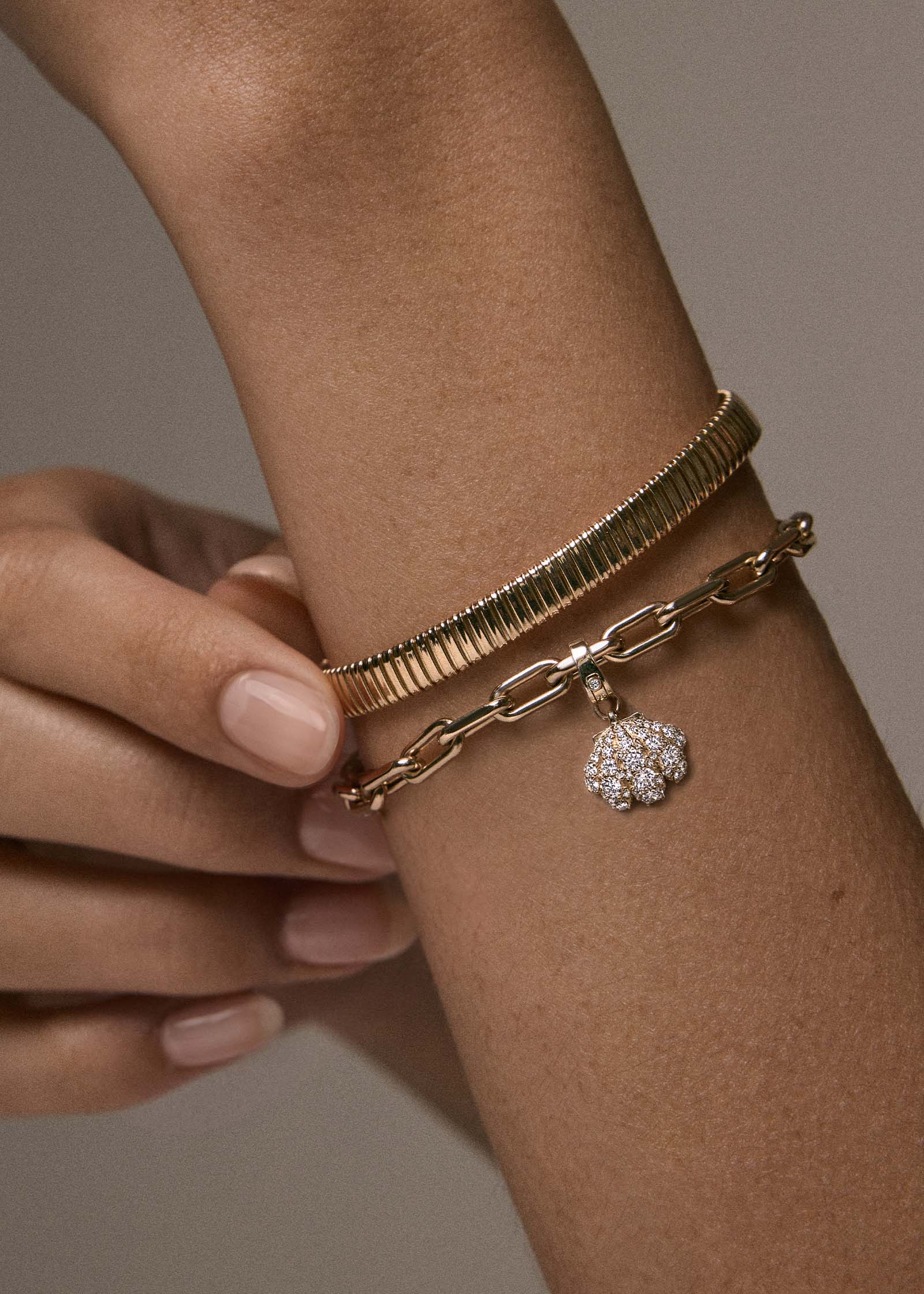 close up of a woman's wrist wearing a Kinn 14k Gold Pavé Diamond Shell Charm Bracelet on Mia Link Chain stacked with a Celina Tubogas Bracelet