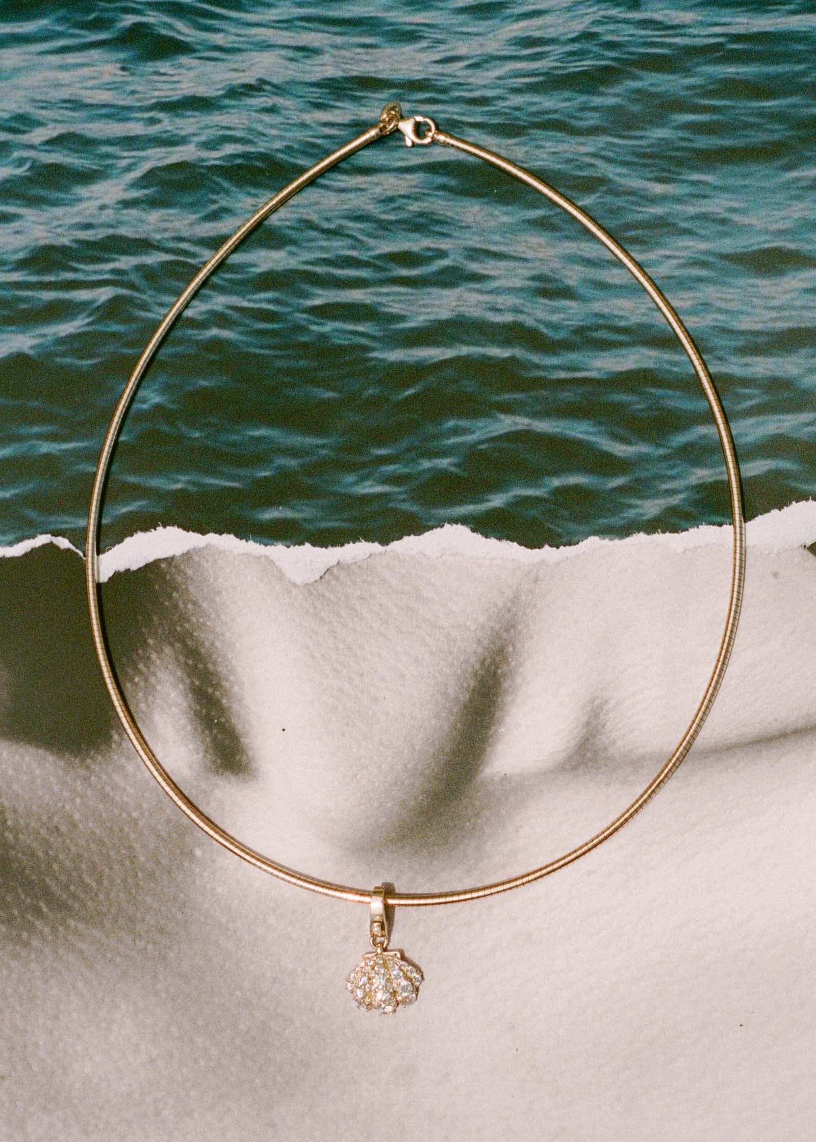 a Kinn 14k Gold Pavé Diamond Shell Charm Pendant on an Heirloom Curved Chain necklace against an image of ocean water