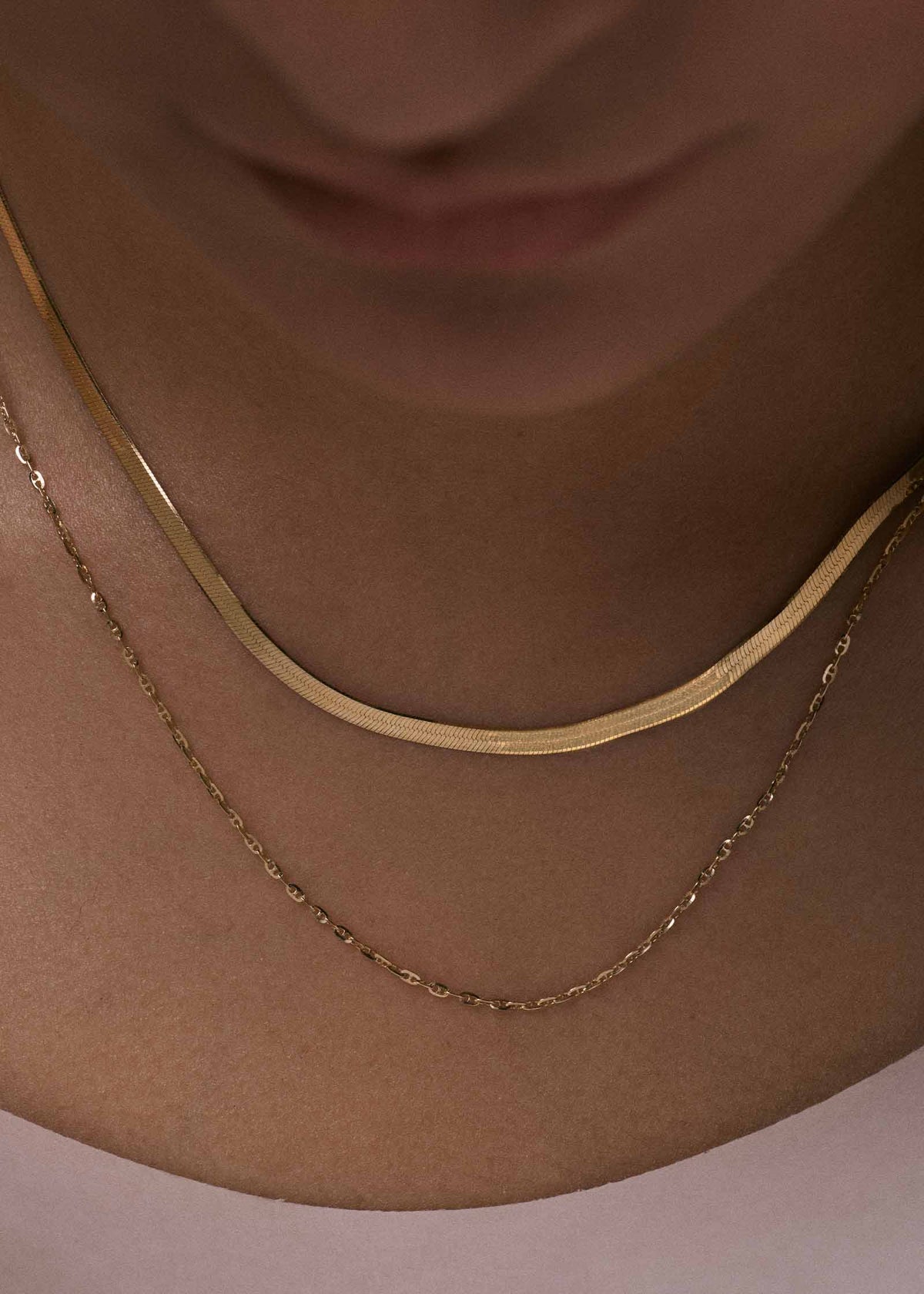 close up of a woman wearing a Kinn 14k Gold Micro Mariner Chain Necklace layered with a Petite Carter Herringbone Chain