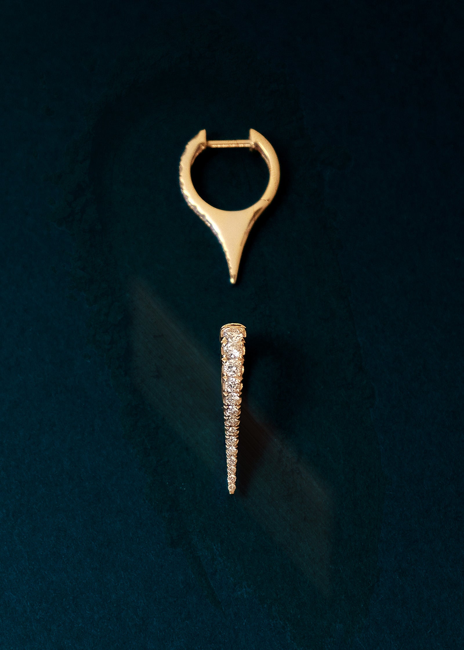 A pair of Kinn x Prince 14k Yellow Gold Point Pavé Diamond Huggies against a blue velvet background with one earring laying upright and the other on its side