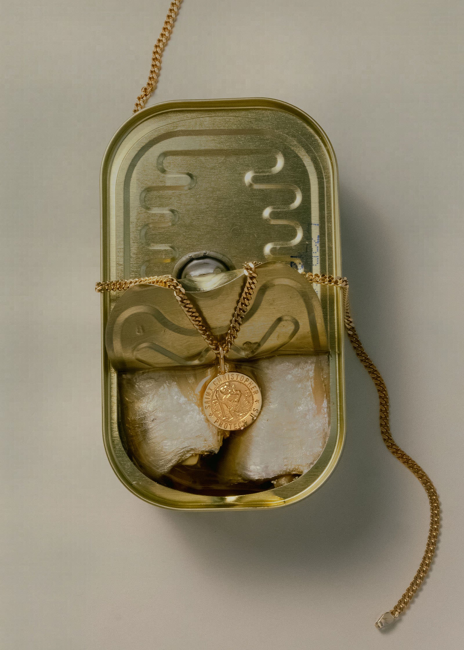 A Kinn 14k Gold Saint Christopher Charm Pendant on a curb chain necklace laying in an open can of sardines