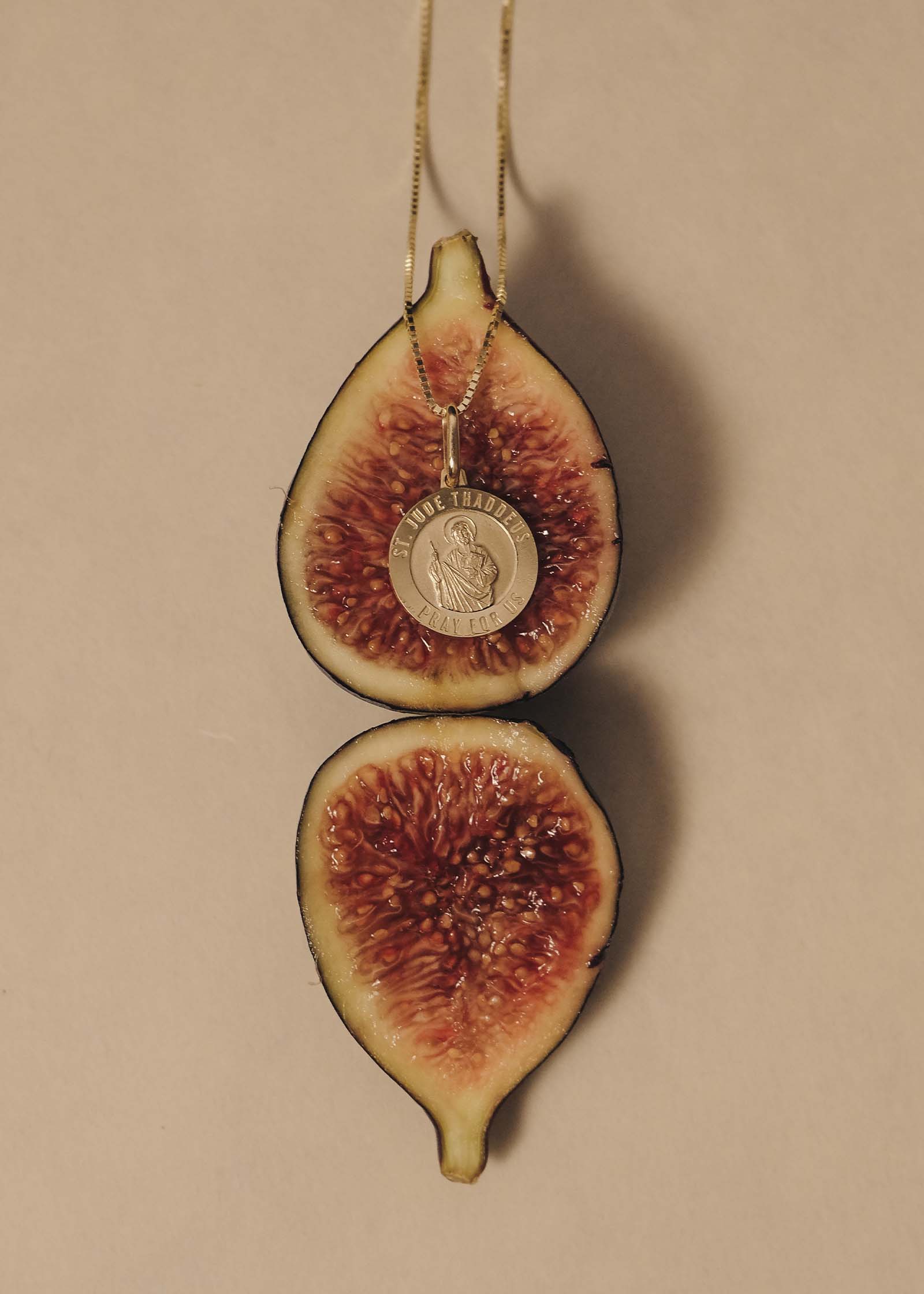 A Kinn 14k Gold Saint Jude Charm Pendant Necklace laying on a fig