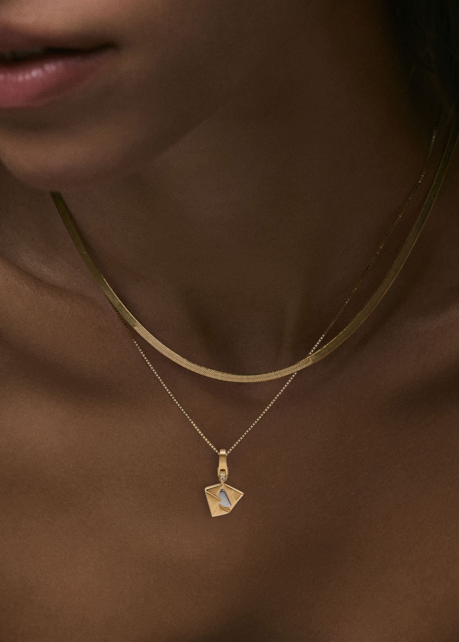 A close up of a woman wearing a Kinn 14k Gold Special Delivery Mail Charm Pendant hanging off a Micro Rolo Chain and layered with a Petite Carter Herringbone Chain Necklace